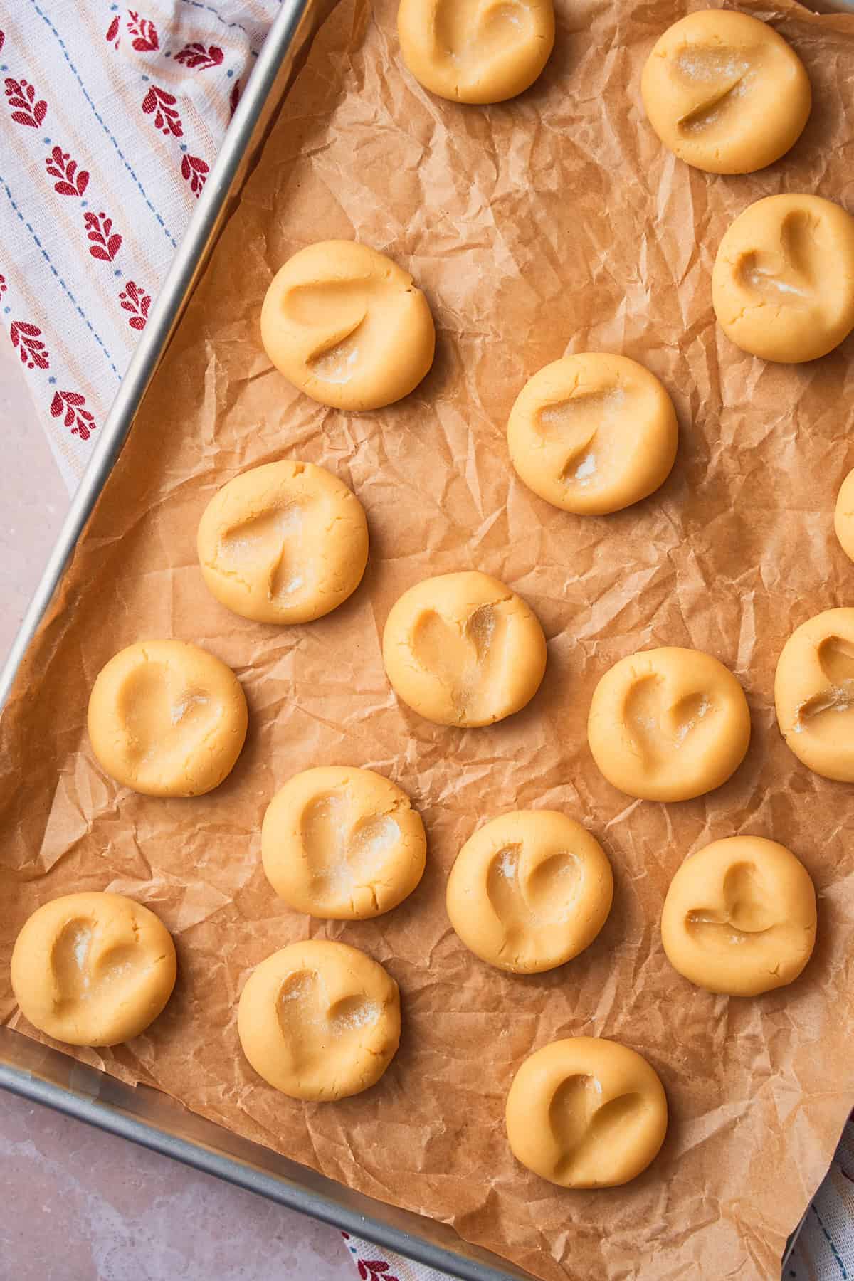 Cookie dough with heart shapes pressed into them on a parchment lined baking sheet.