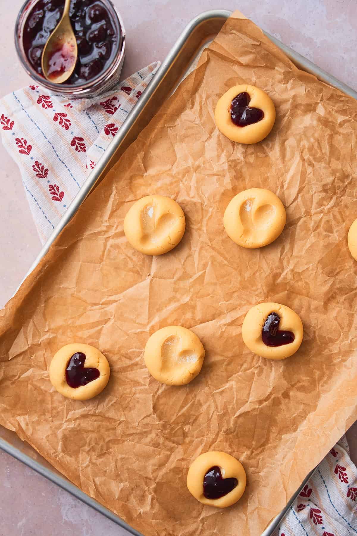 Half of of the heart shaped cookies filled with jam on a baking sheet lined with parchment getting ready to bake. 