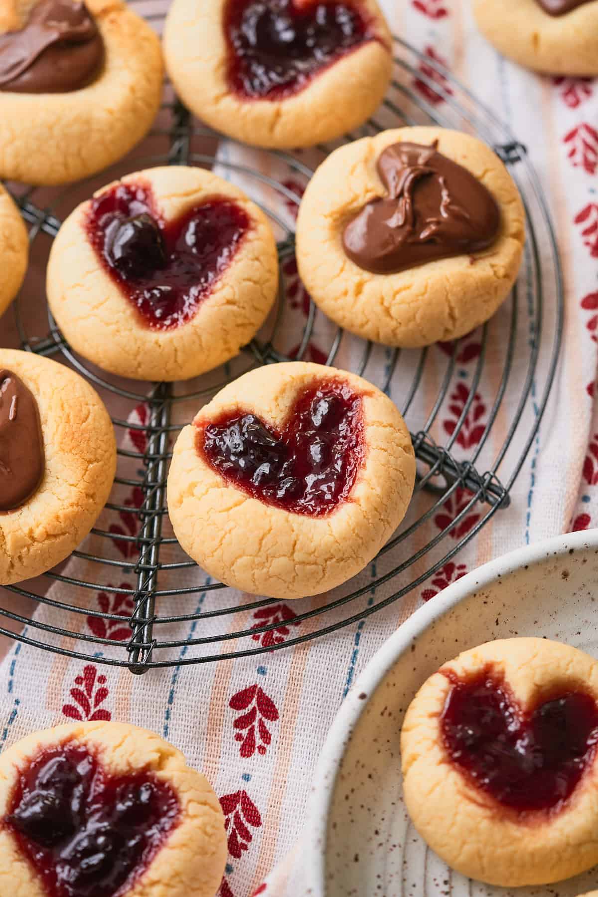 Very close up macro shot  of thumbprint cookies with little heart shapes filled with cherry jam and nutella on wire cooling racks. 