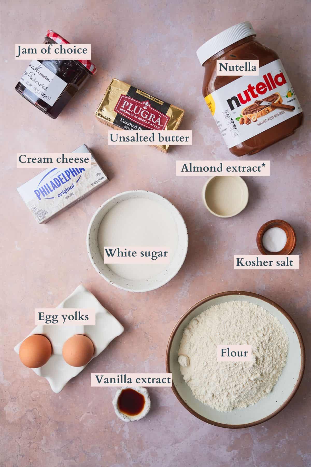 Ingredients to make heart shaped thumbprint cookies laid out on a table and labeled to denote each ingredient. 