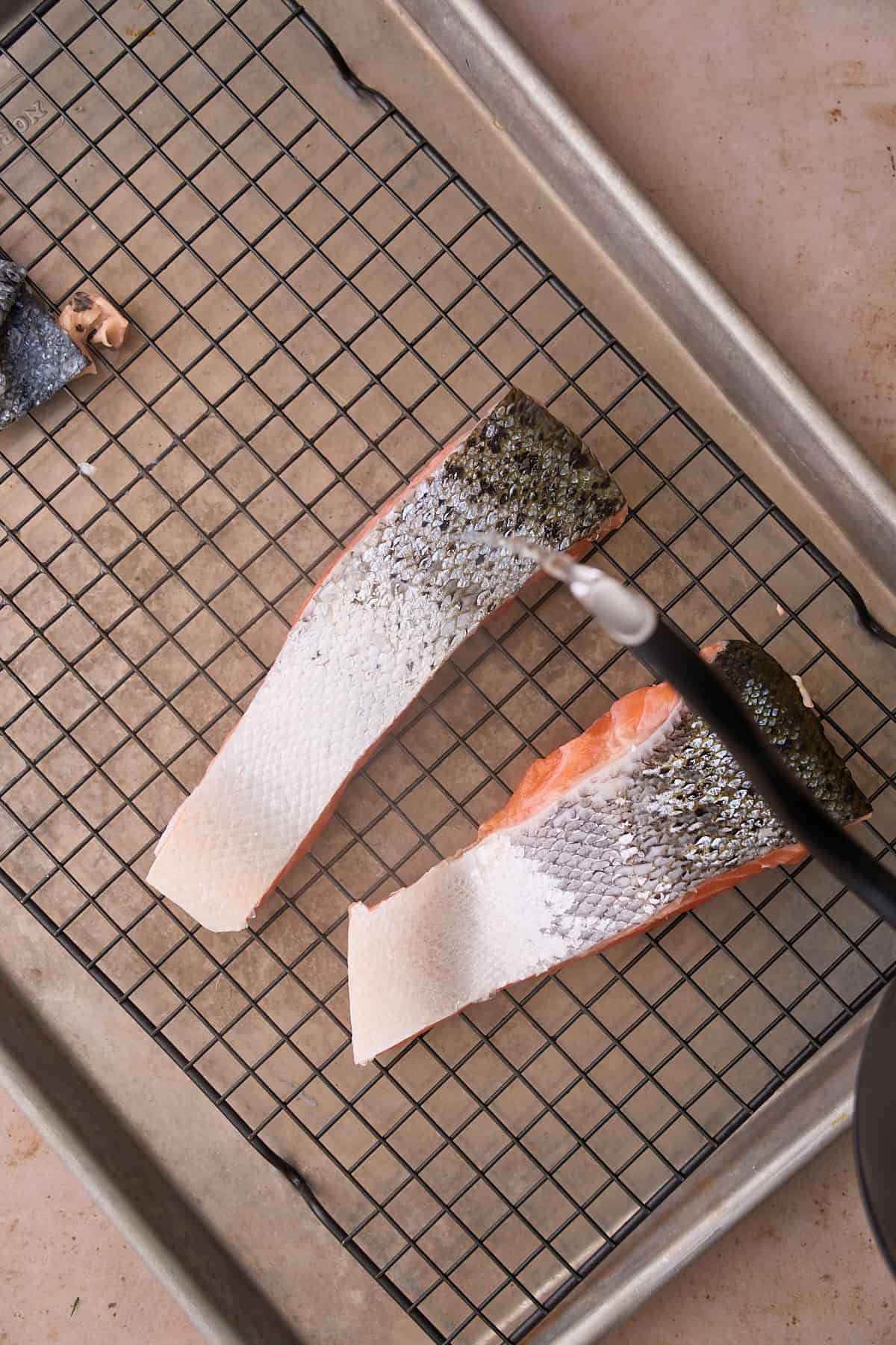 Boiling hot water pouring over top of salmon skin on a cooling rack over top of a baking pan. 