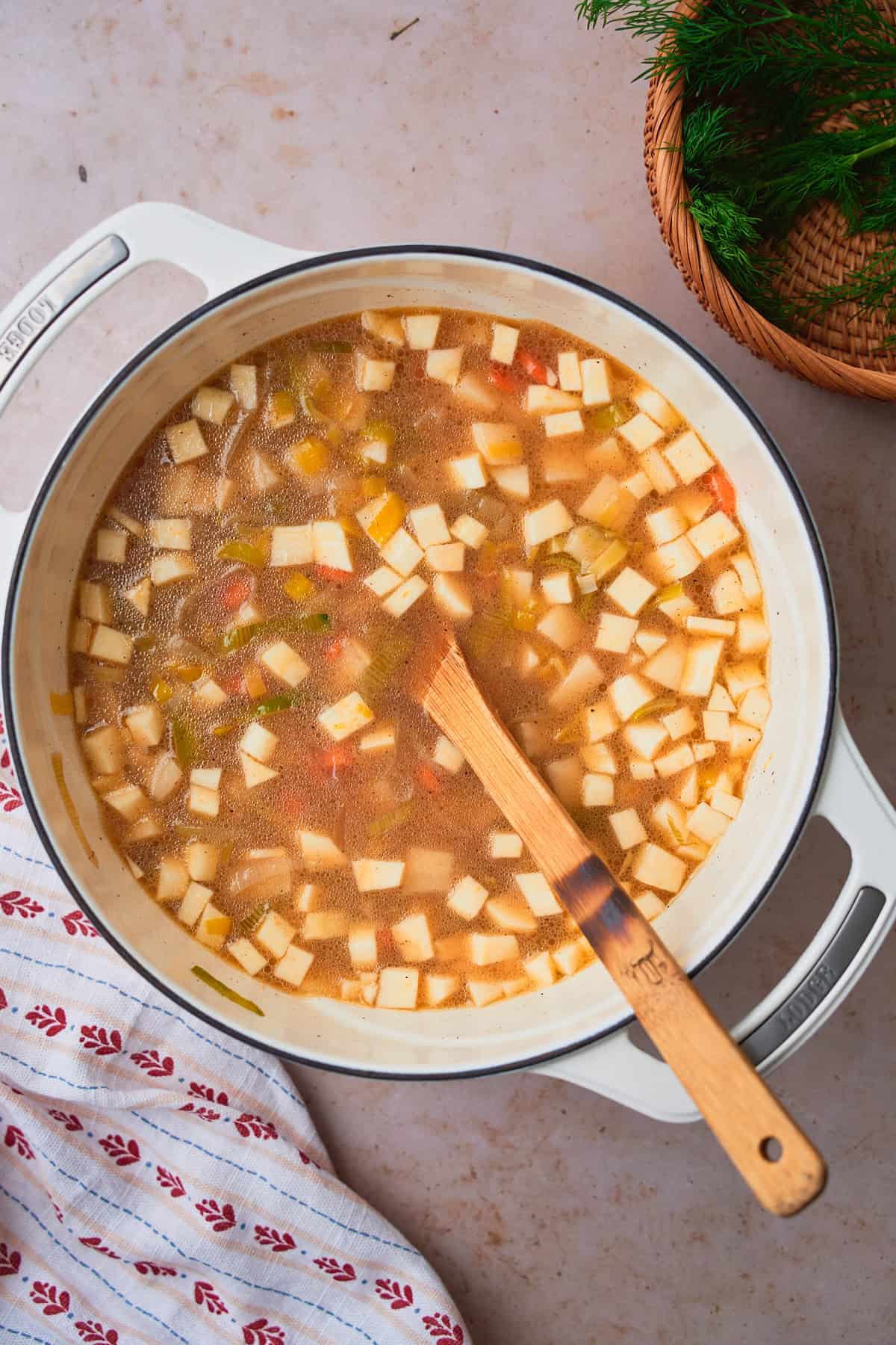 Parsnips, carrots, and potatoes added to a stockpot with fish stock and leeks to simmer into a soup. 
