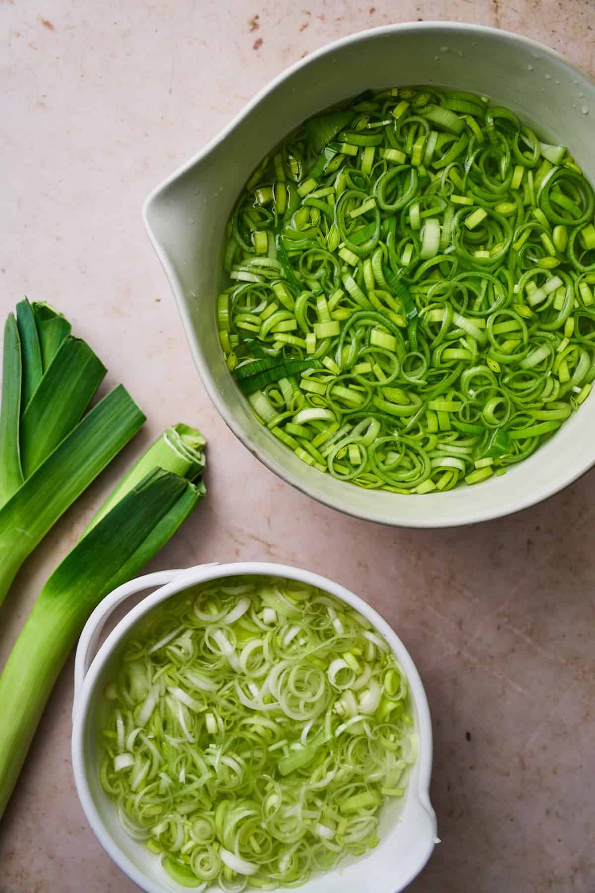 Light and dark green parts of leeks separated from each other in bowls of water getting cleaned. 