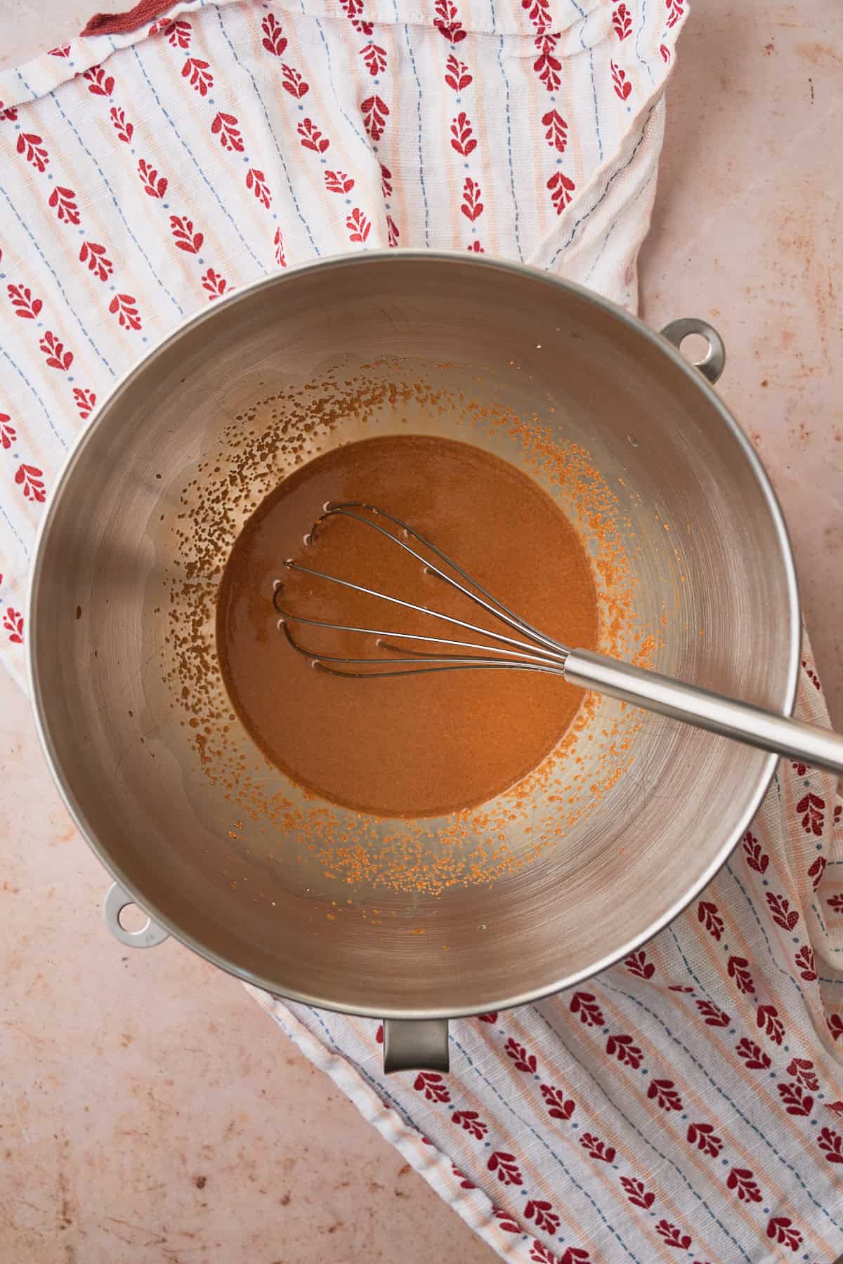 Molasses, eggs, milk, and butter added to a mixing bowl with a whisk overtop of a cute linen napkin with little heart shapes on it. 