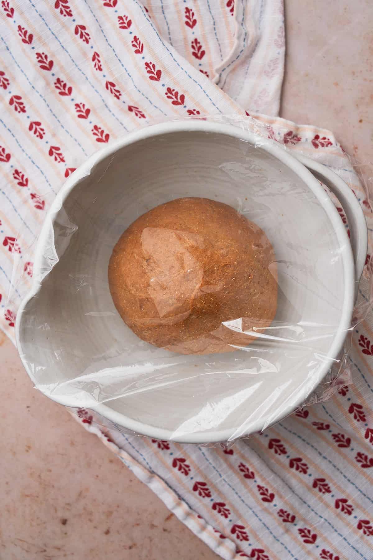 Ball of rye bread dough in a bowl covered with plastic wrap.