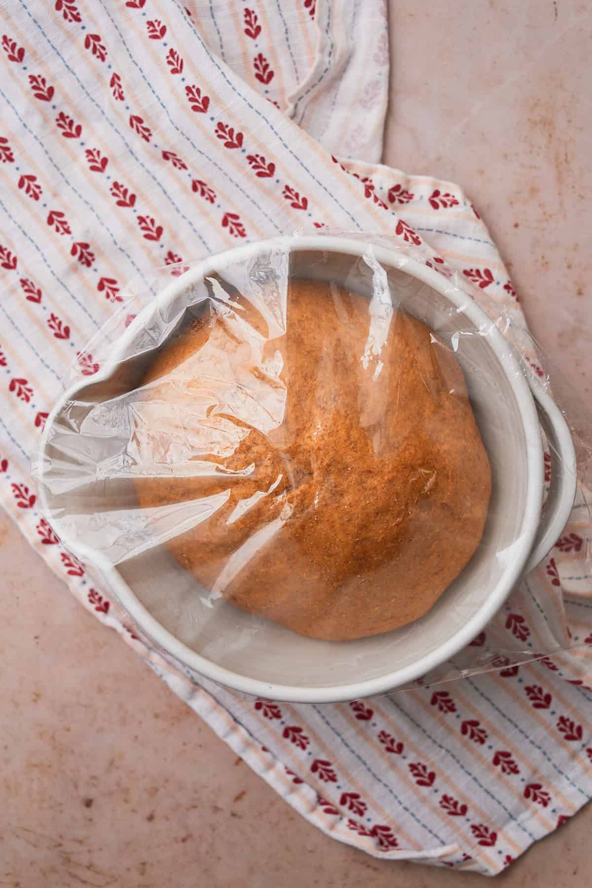 Fluffy, pillowy soft rye bread dough risen in a bowl covered with plastic wrap. 