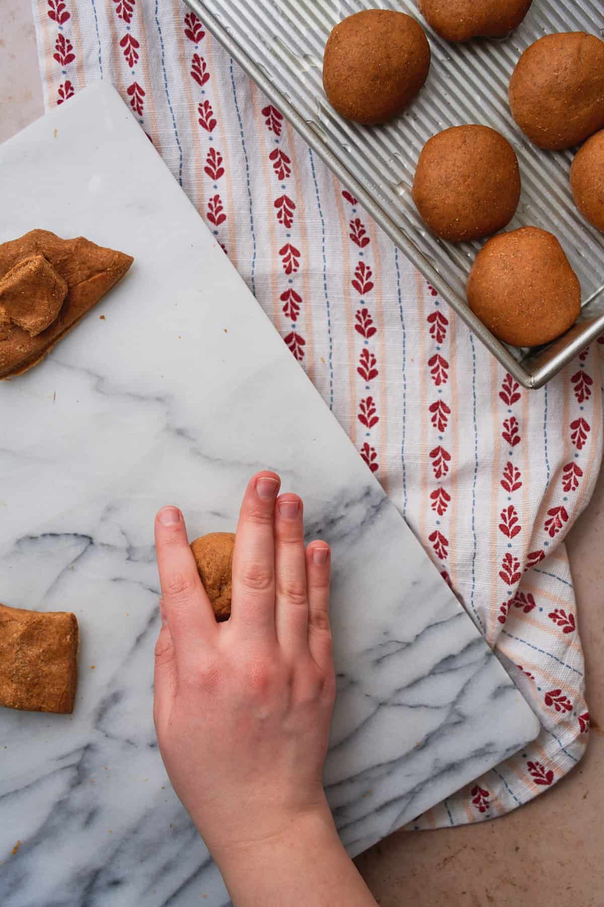 Hands rolling a ball of dough on a marble work surface to make it into a round ball shape. 