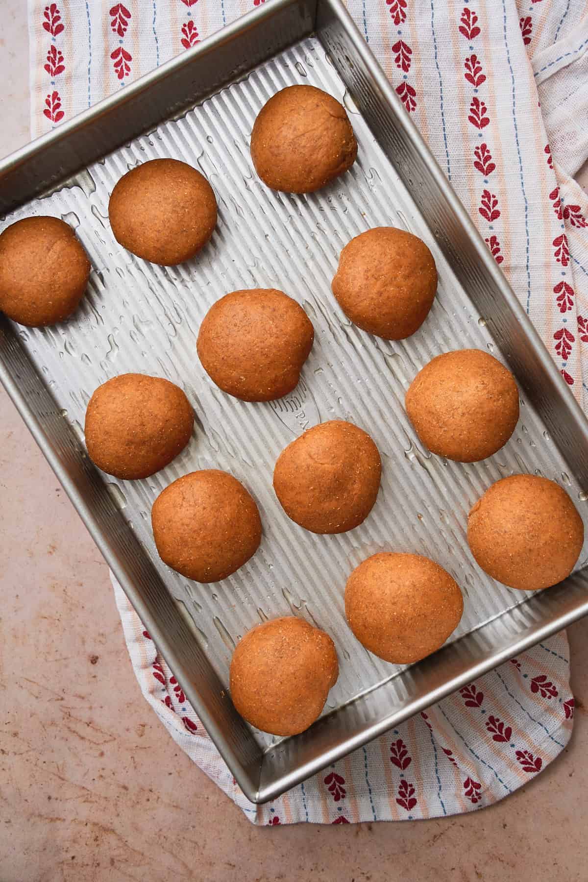 Rye bread balls in a greased baking sheet getting ready to rise again. 