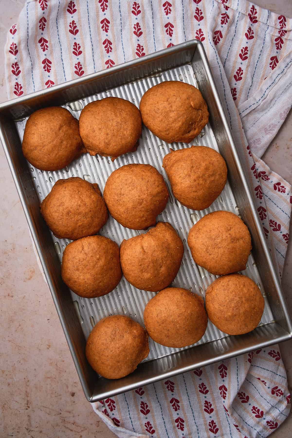 Puffy, risen rye rolls in a baking dish. 