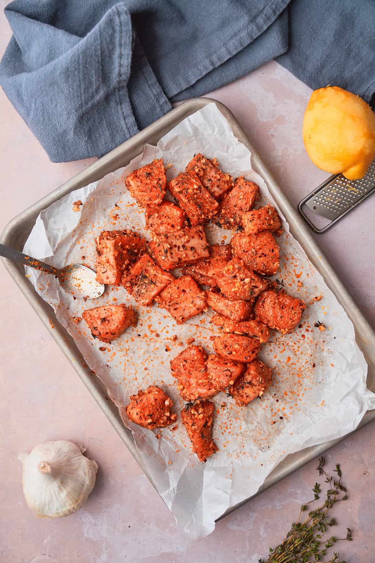 Salmon bites on a parchment lined baking sheet seasoned with garlic, lemon zest, and other seasonings. 