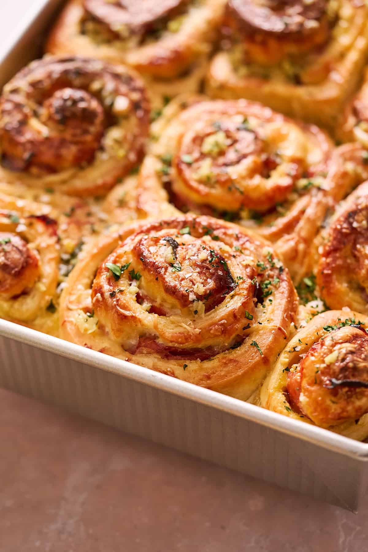 Ham and Cheese Rolls Close up shot of baked ham and cheese yeasted rolls in a metal pan, brushed with parsley garlic butter.