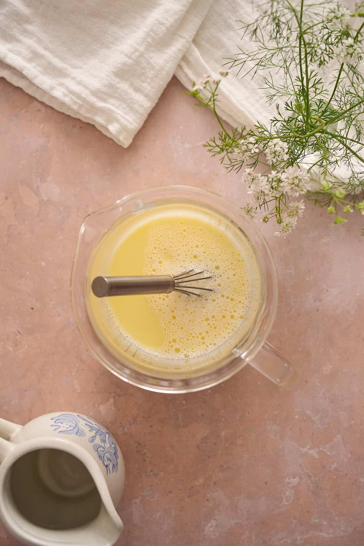 Melted butter and milk being whisked together in a glass beaker.