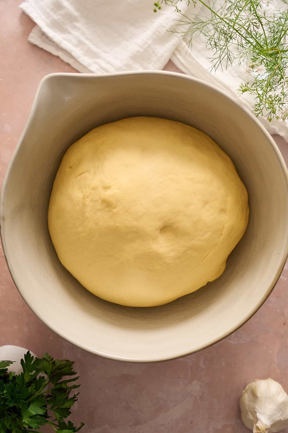 Puffy dough in a bowl with a small indent where it has been pressed. 