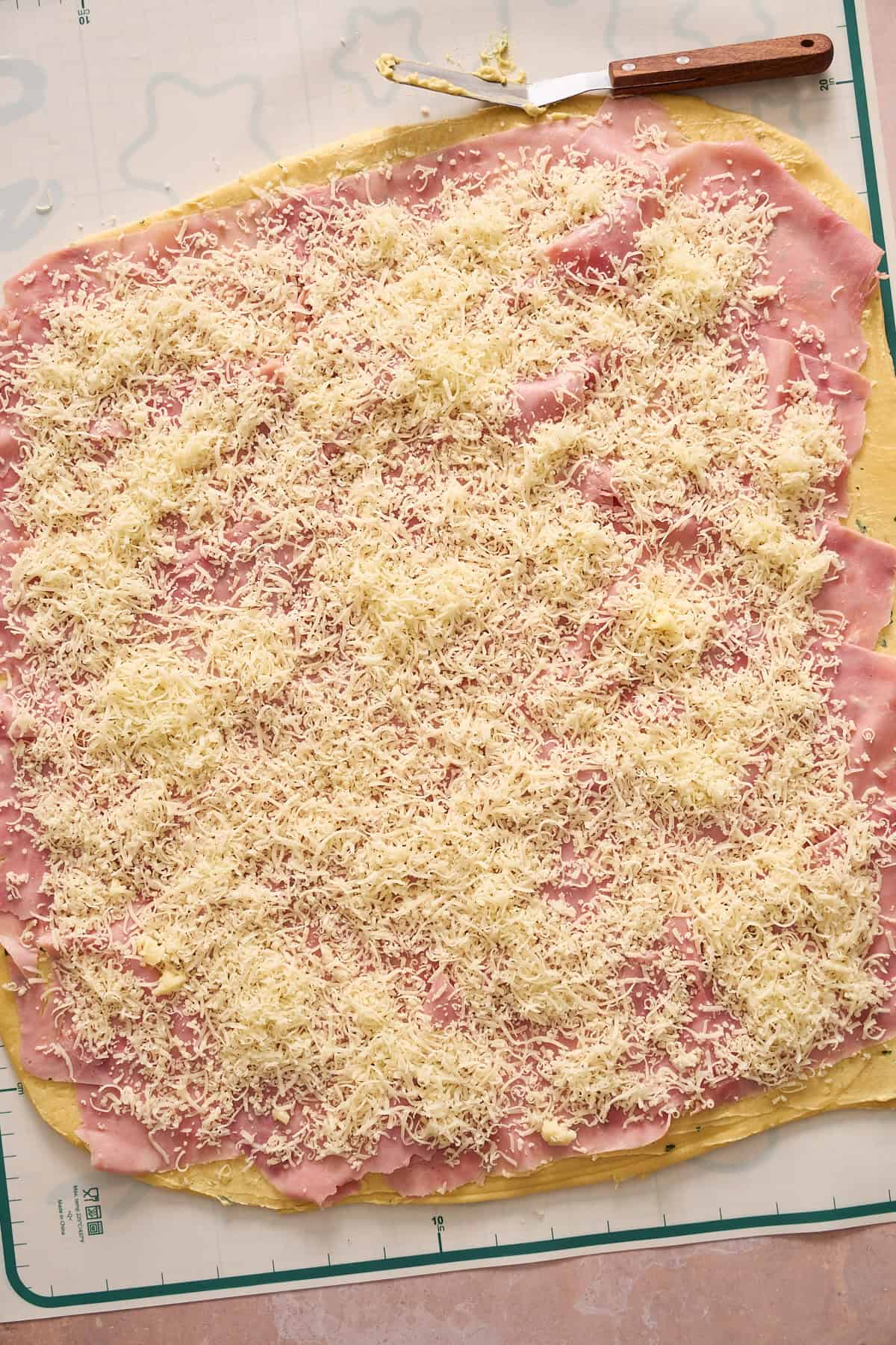 Thin layer of ham, covered by shredded cheese on top of a buttery topping on the inside of a rolled out dough. 