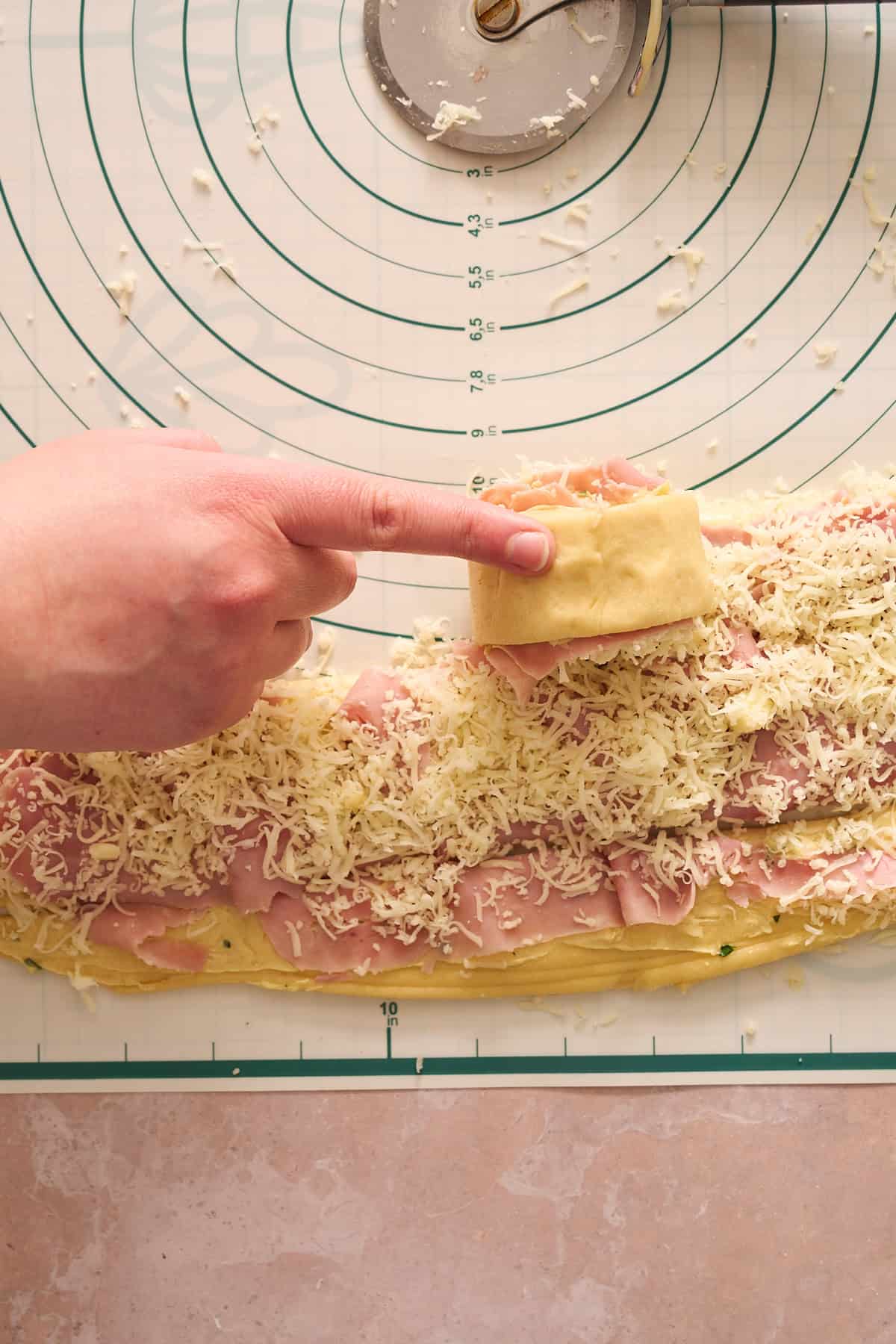 Hand tightly rolling a ham and cheese roll on a silicone mat. 