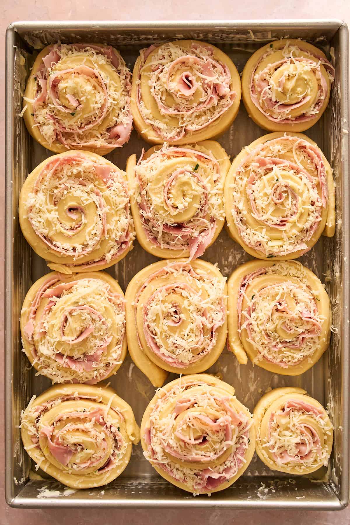 Raw ham and cheese rolls in a pan getting ready for a second rise. 