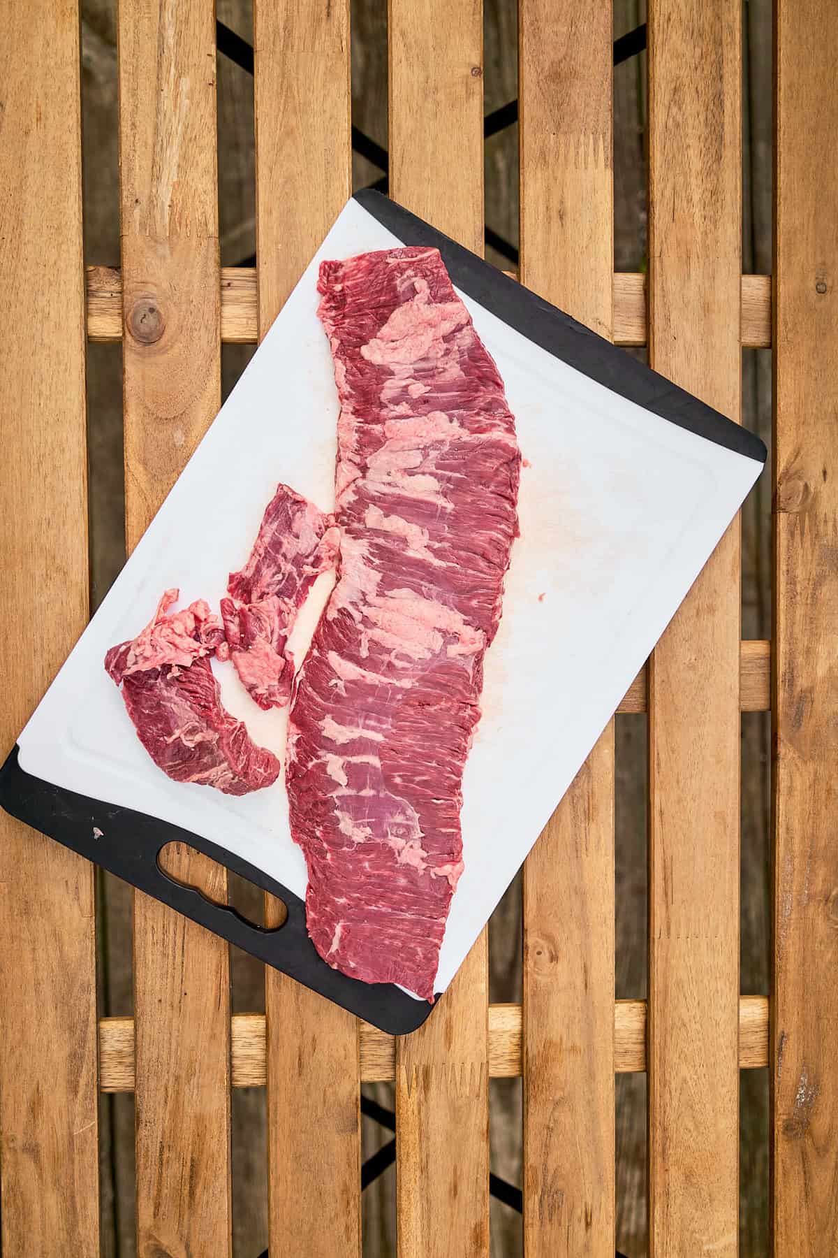 Skirt steak on a plastic cutting board pounded thin with a meat mallet and with the ends cut off of the steak.