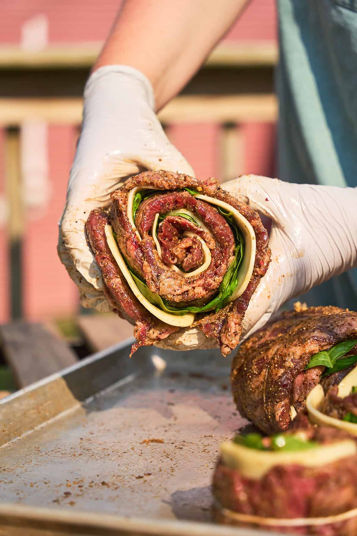 Steak rolled and shaped like pinwheel stuffed with cheese and spinach being held by two gloved hands.