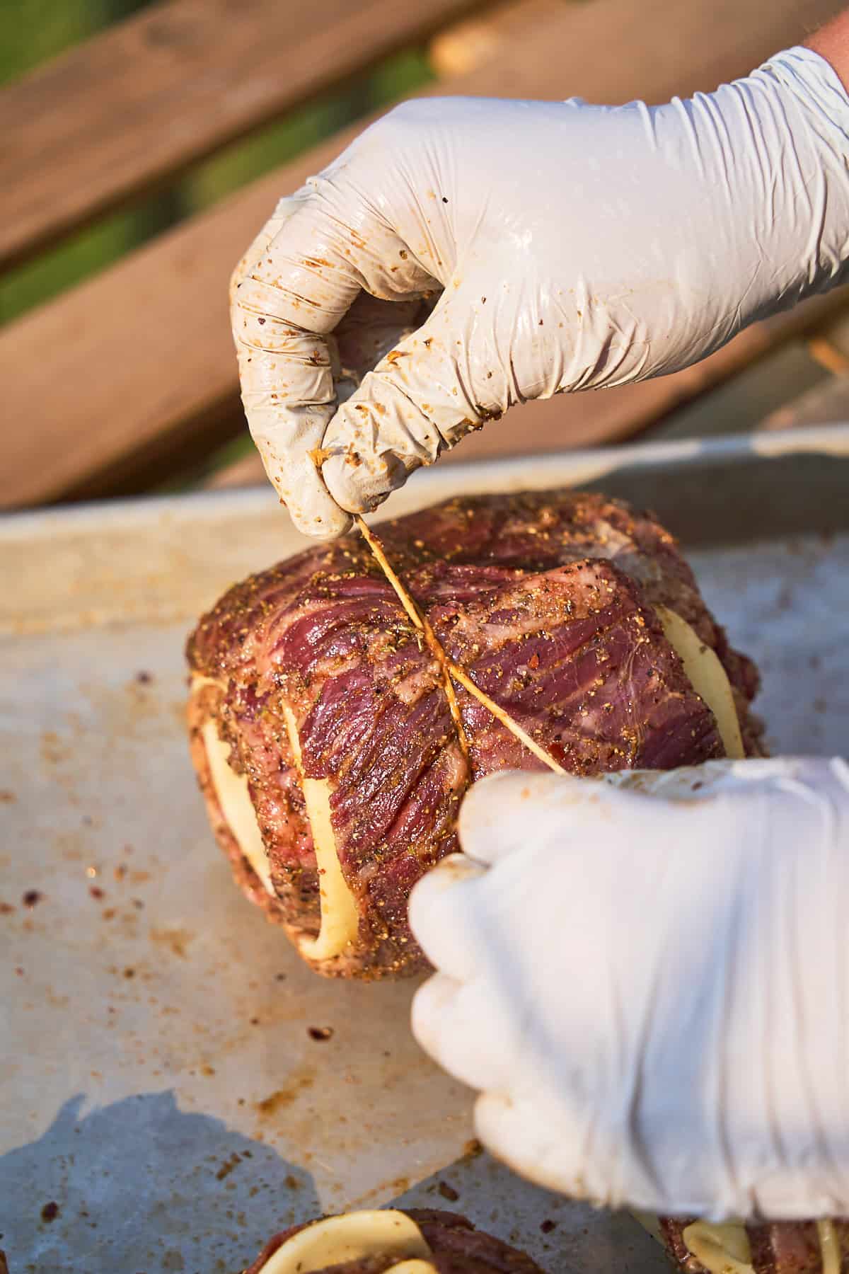 Gloved hands tightly tying steak pinwheels with twine.