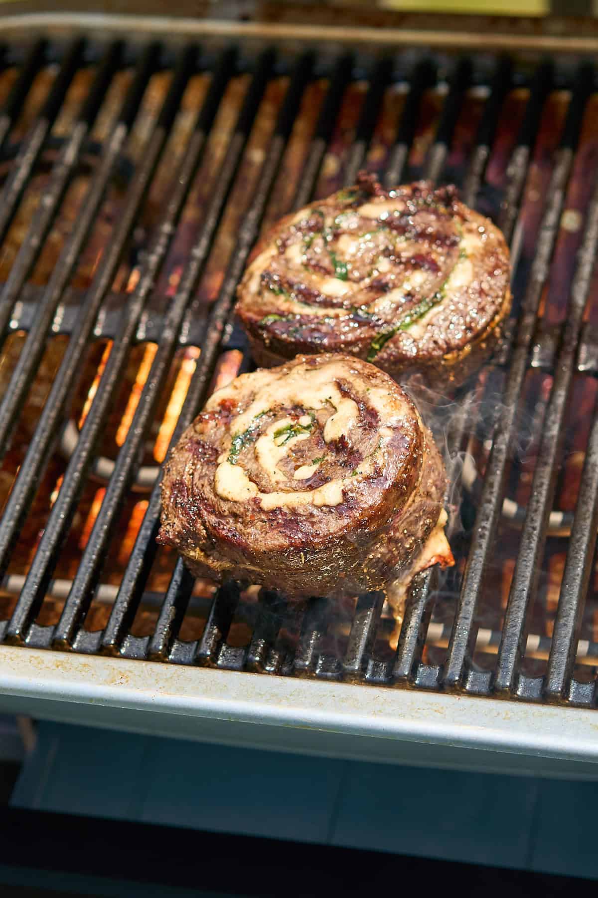 Steak pinwheels cooking on a hot grill with grill marks showing and cheese oozing out.