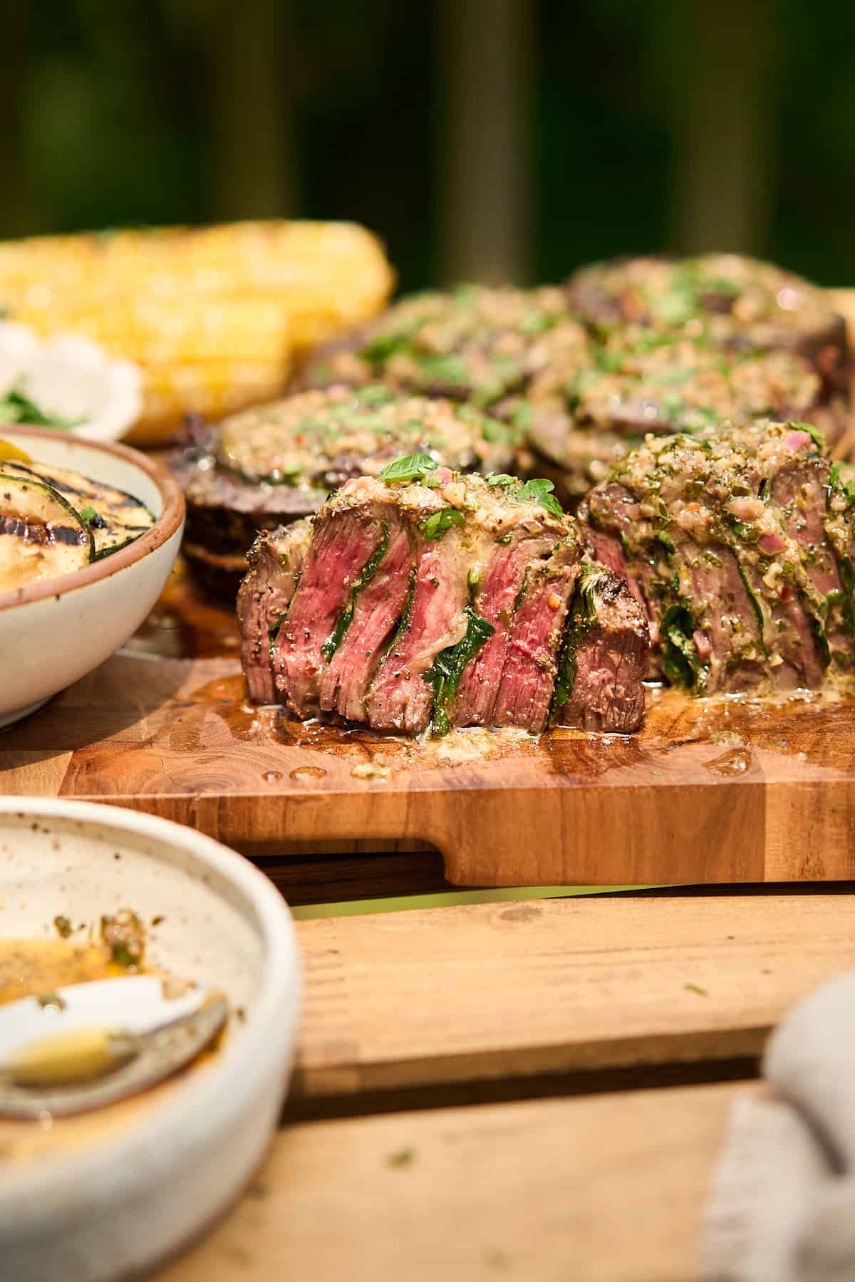 Shot of a steak pinwheel cut in half to show the interior and a perfect cook surrounded by cowboy butter, corn on the cob, and zucchini.