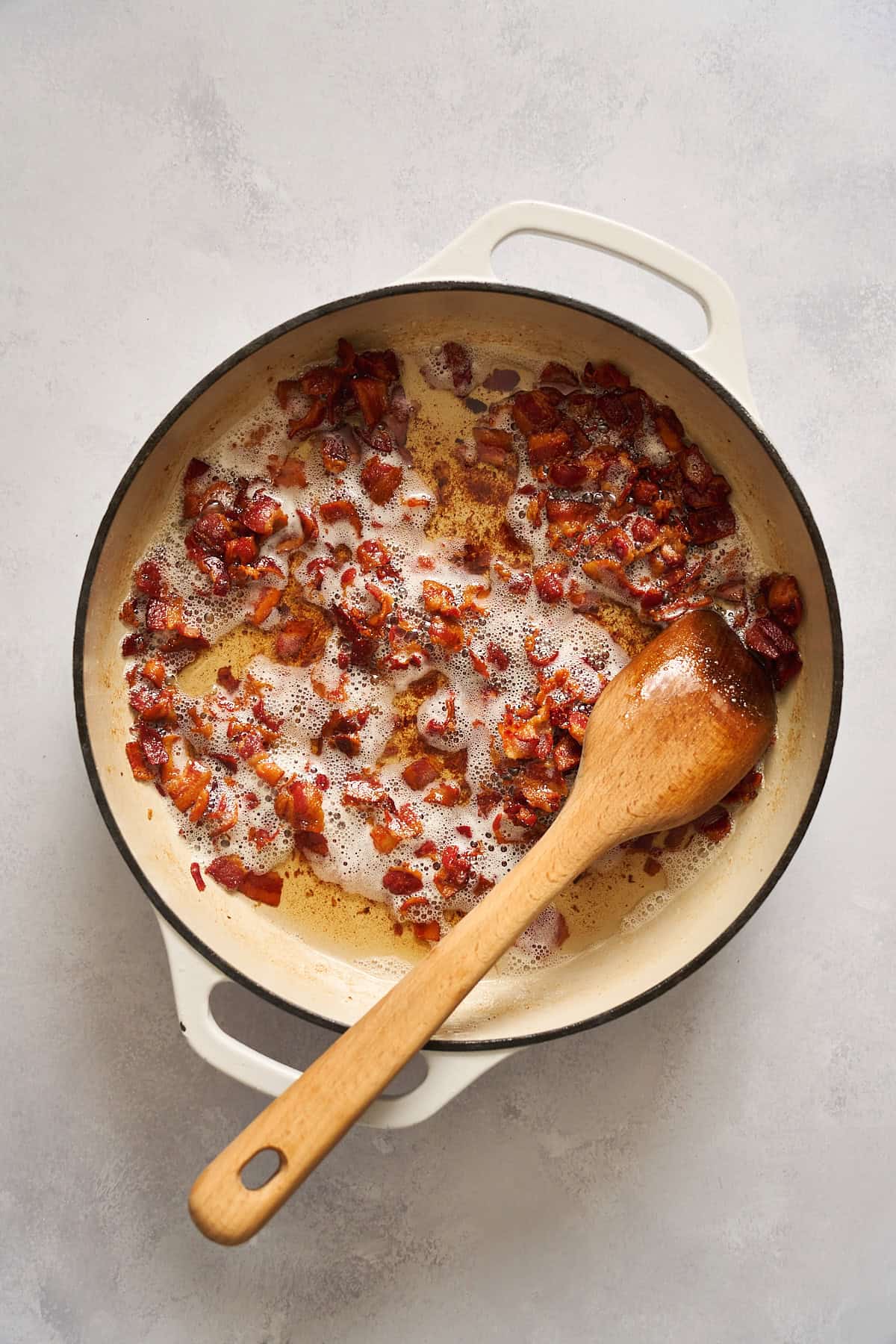 Cooked bacon pieces in a skillet with a wooden spoon used to stir it.
