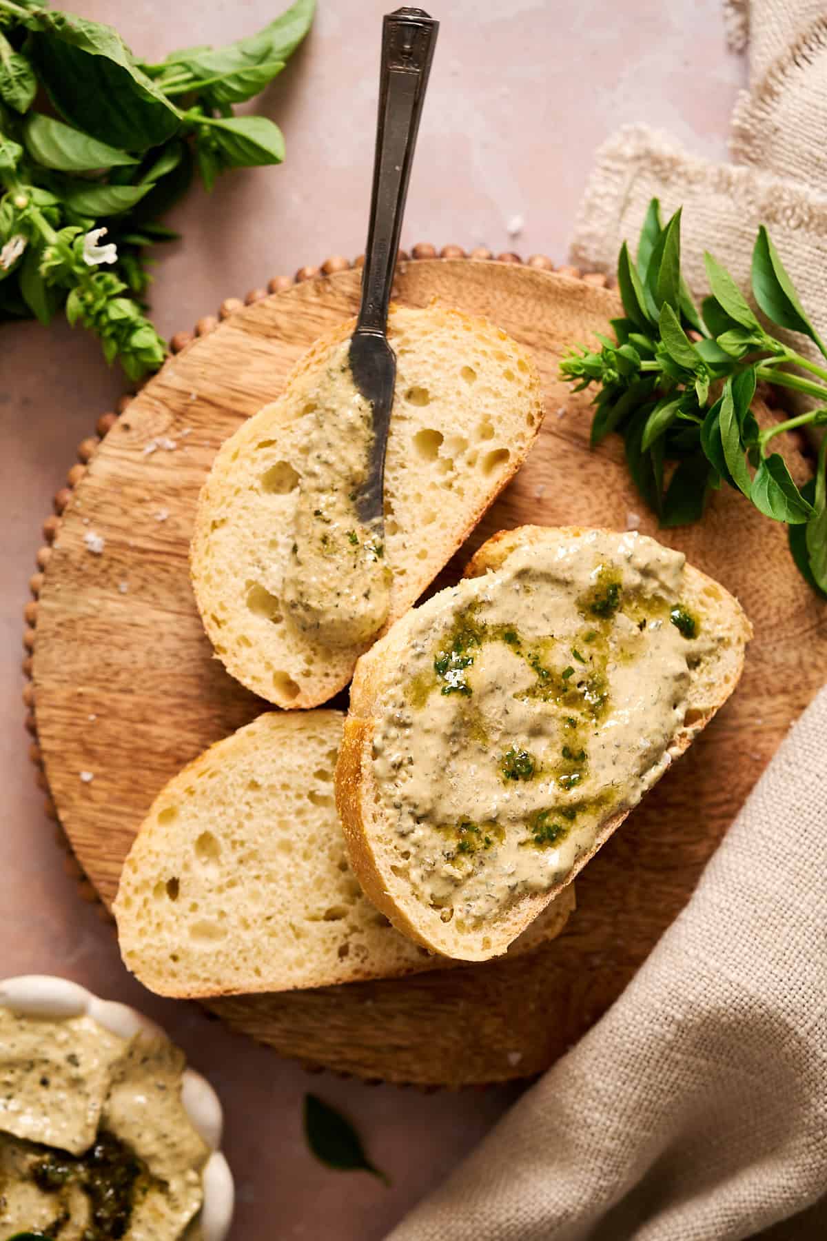 Basil pesto butter spread onto bread slices and surrounded by fresh basil.