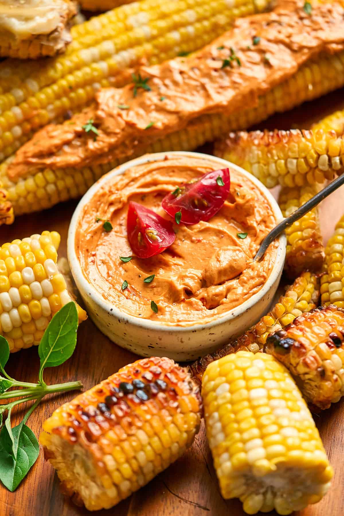 Ramekin of tomato butter topped with fresh tomatoes surrounded by corn on the cob in various forms.