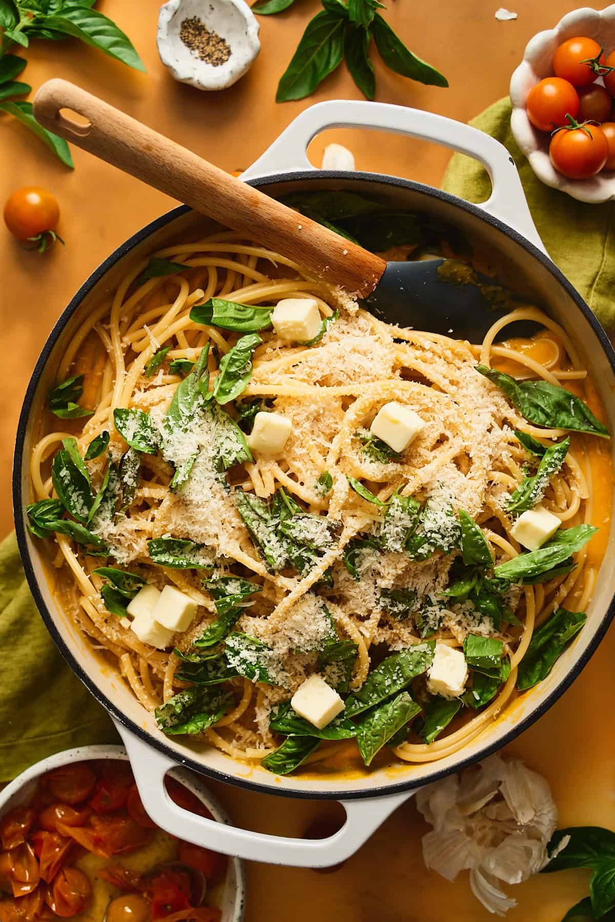 Cooked pasta in a large dish with parmesan, basil, sauce, and butter chunks.