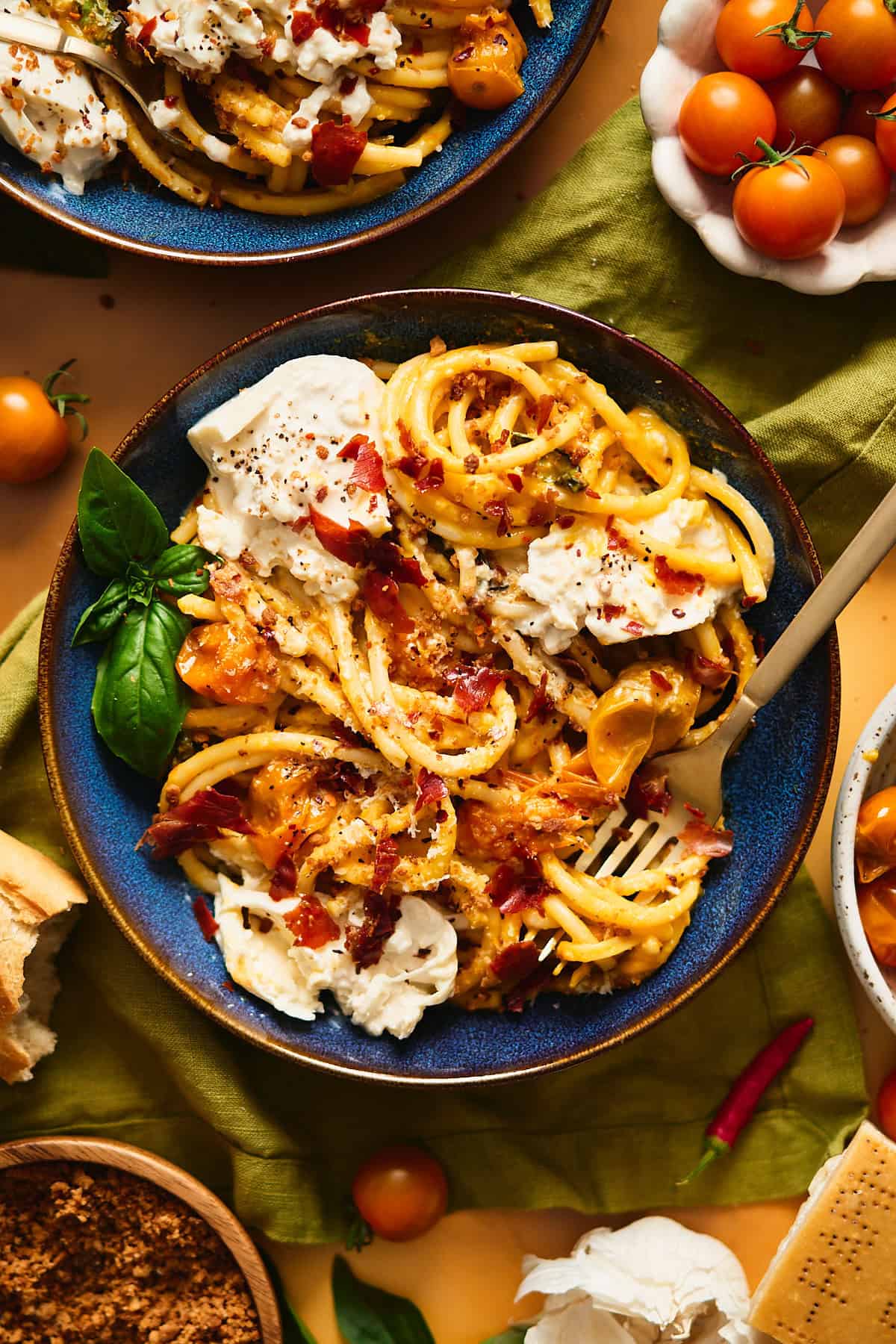 Close up shot of a bowl of roasted Sungold tomato pasta topped with creamy burrata cheese and crispy prosciutto pieces.