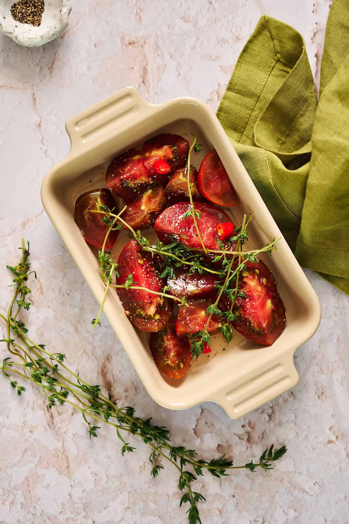 Tomato pieces in a baking dish with thyme sprigs over top and drizzled with oil.