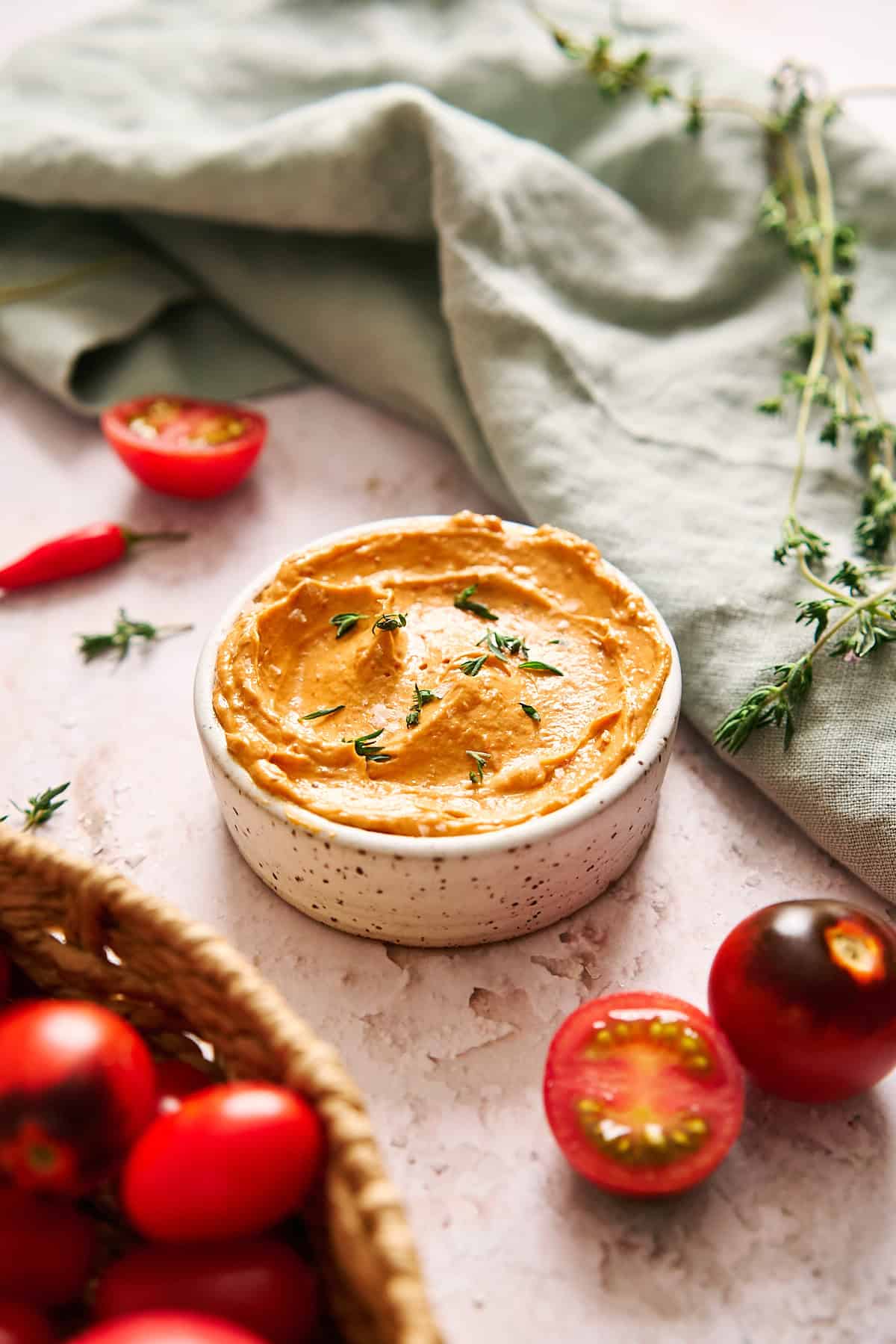 45-degree shot of a ceramic white dish with sliced and whole tomatoes surrounding, and a light blue linen.