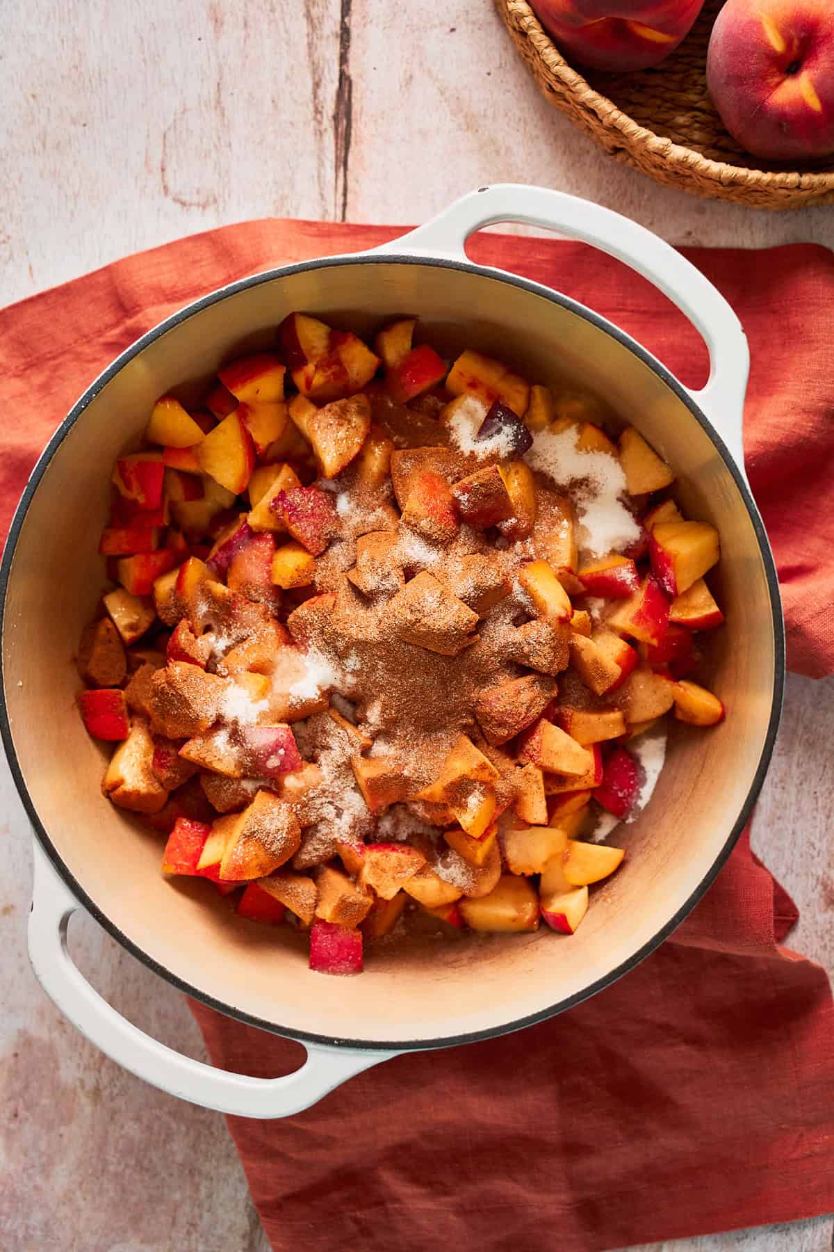 Peaches, cinnamon, and sugar in a Dutch oven on top of a terra cotta linen napkin.