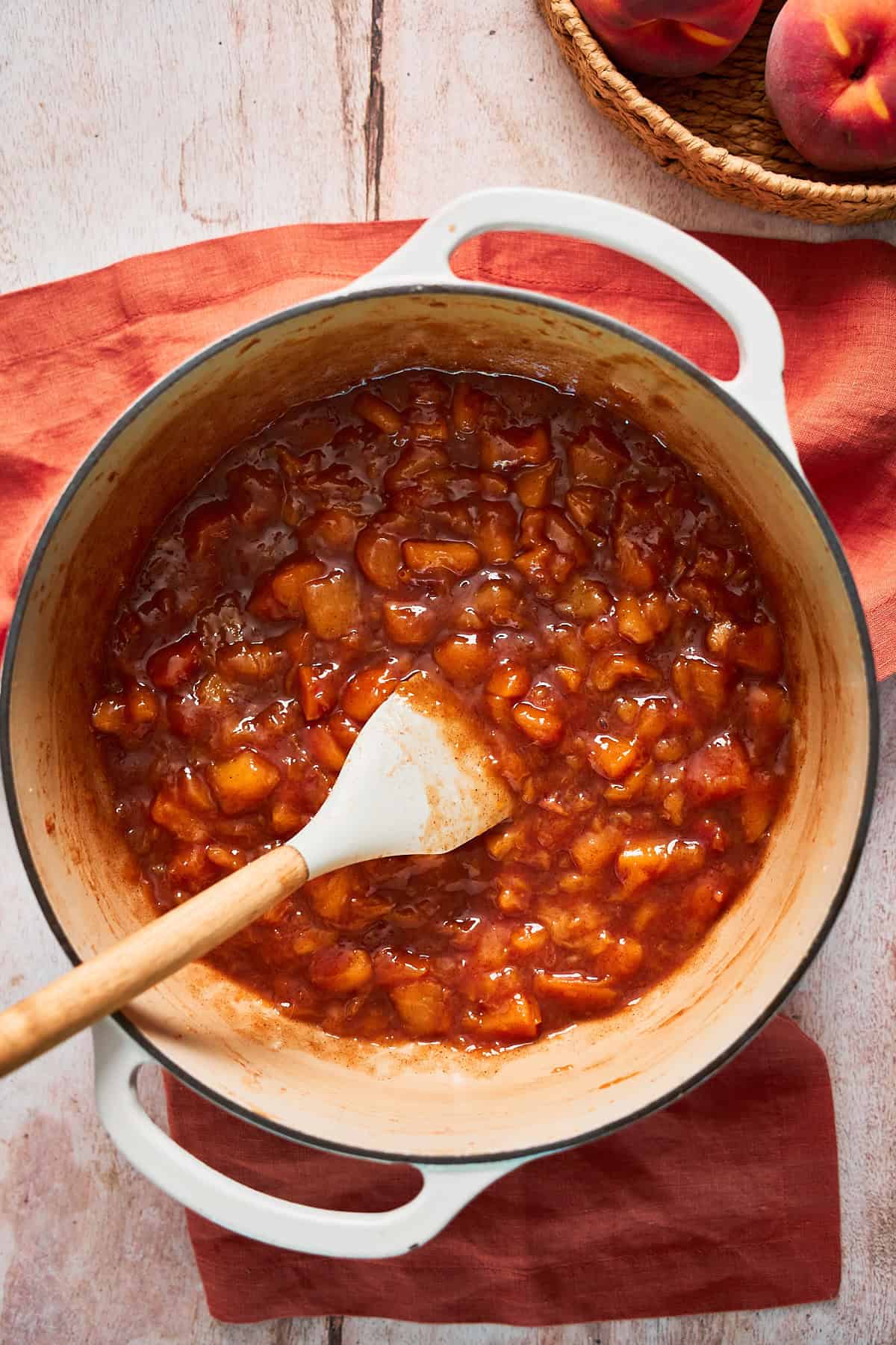 Cooked chunk peach jam in a large Dutch over with a rubber spatula mixing the ingredients together.