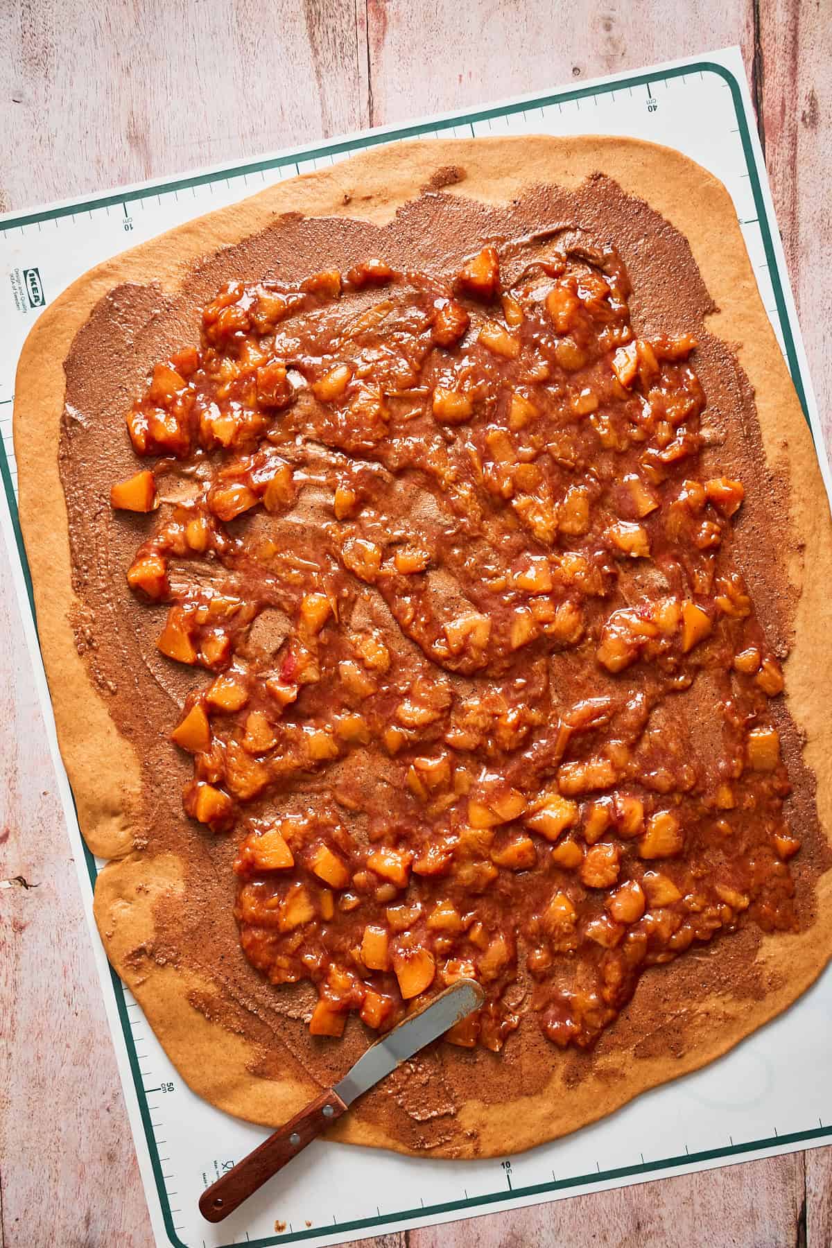 Peach filling spread overtop of brown sugar filling on cinnamon roll dough.