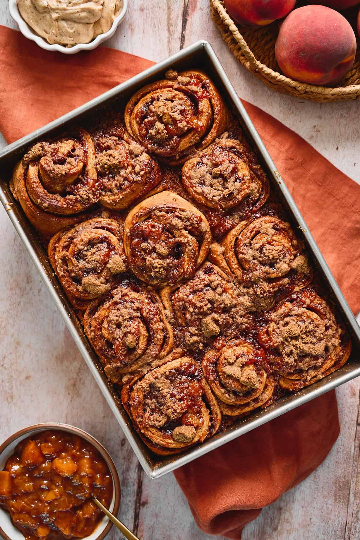 Baked peach cobbler cinnamon rolls in a square baking pan on a terra cotta linen.