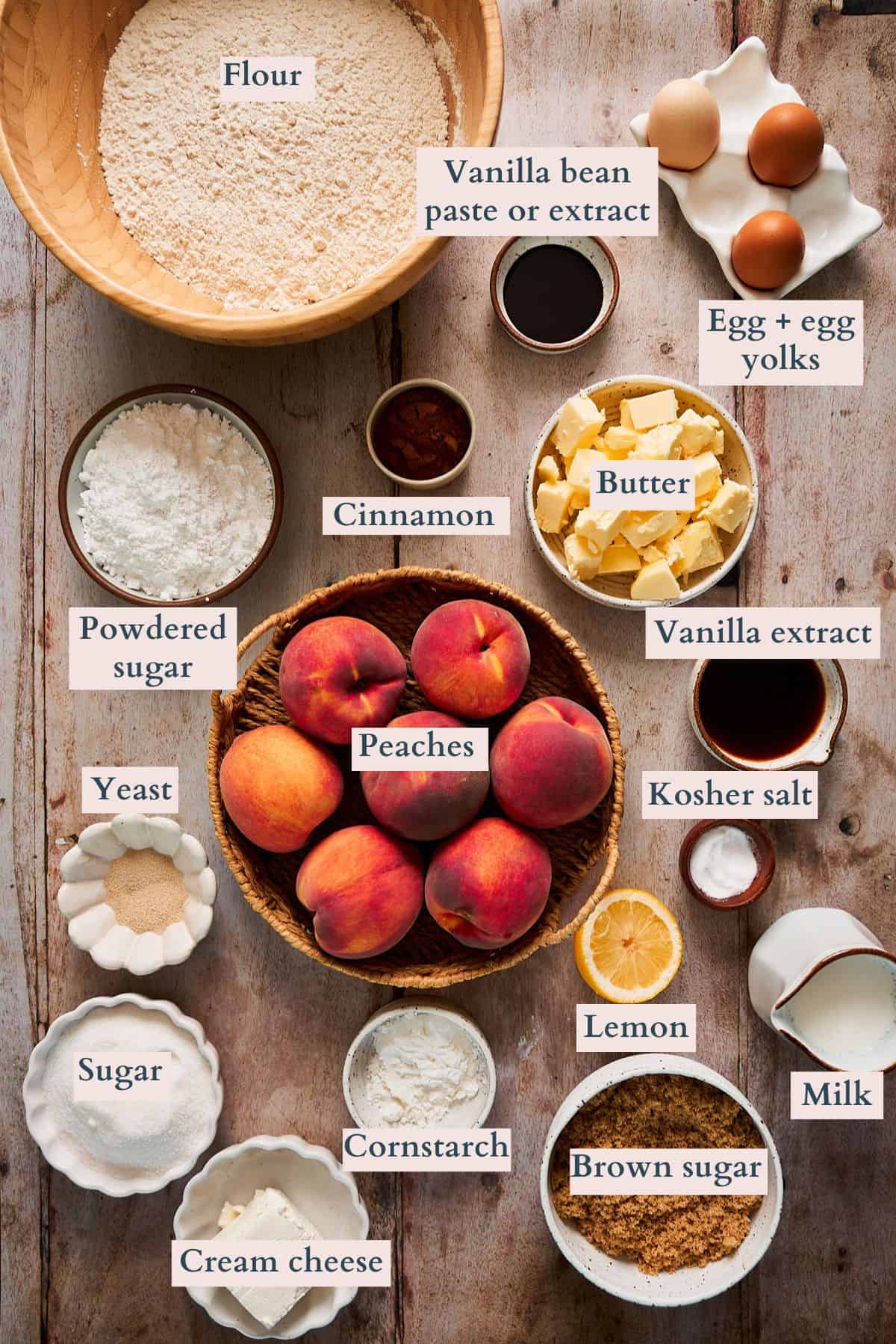 Ingredients to make peach cobbler cinnamon rolls laid out on a table and labeled to denote each ingredient.