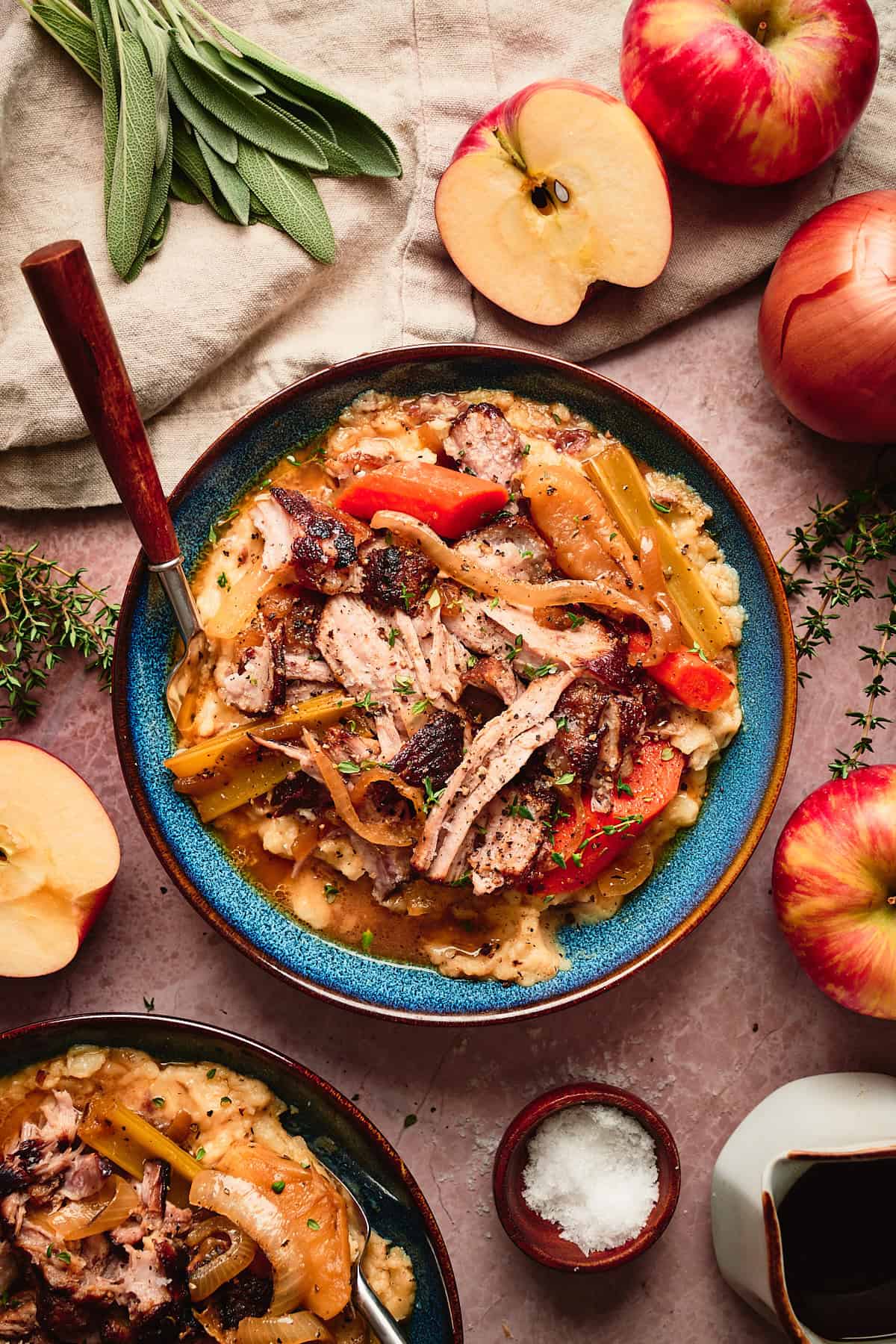 Close up overhead shot of apple cider pork pot roast over mashed potatoes surrounded by fresh apples and herbs.
