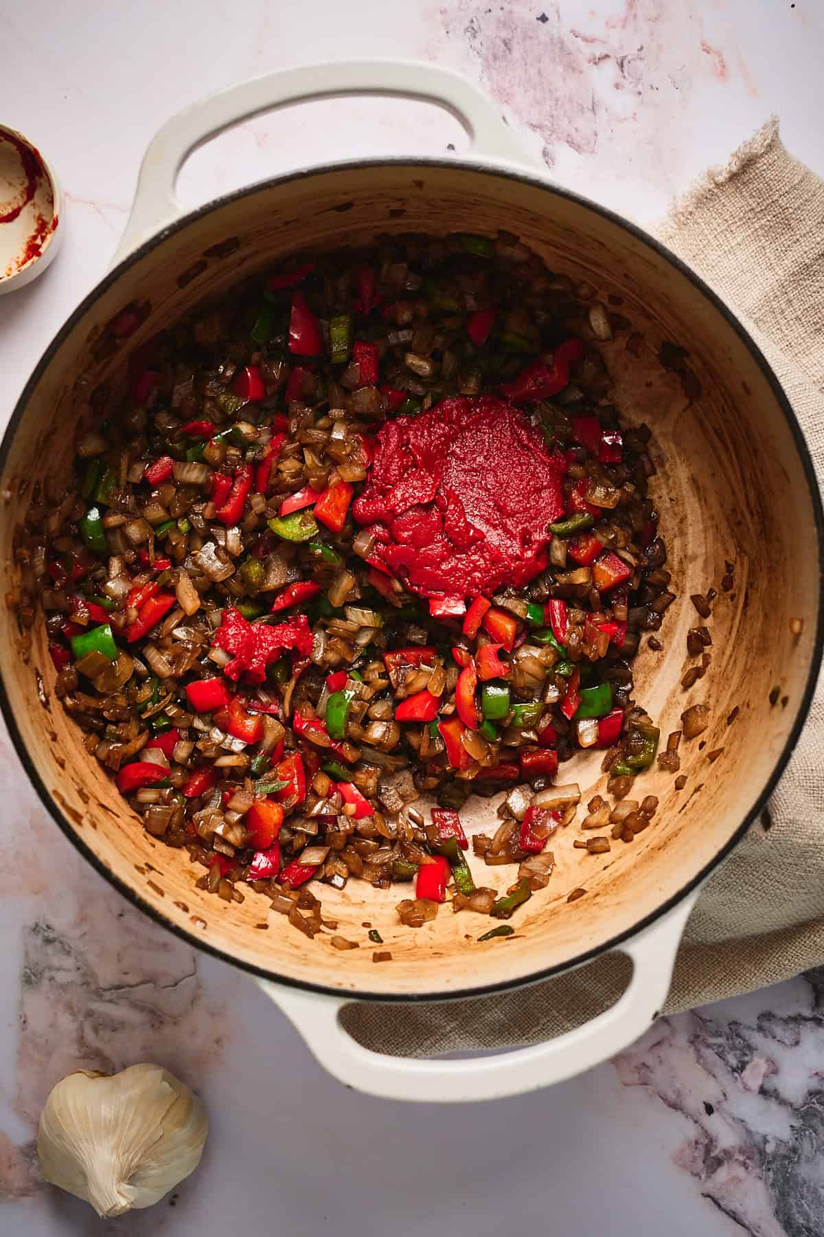Onions and peppers cooking in a Dutch oven with tomato paste added to the top.