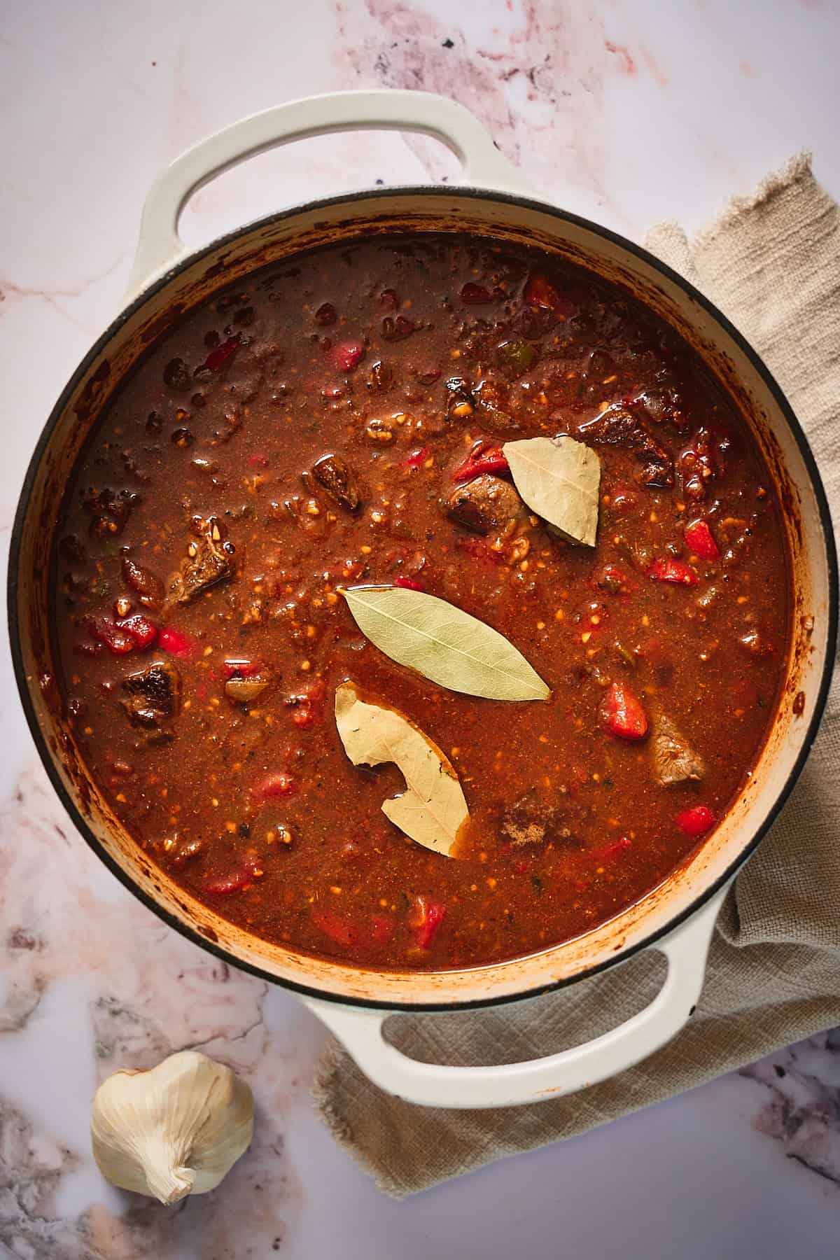 Liquid, beef, tomatoes, and bay leaves added to a Dutch oven to begin a long simmer to make chili.