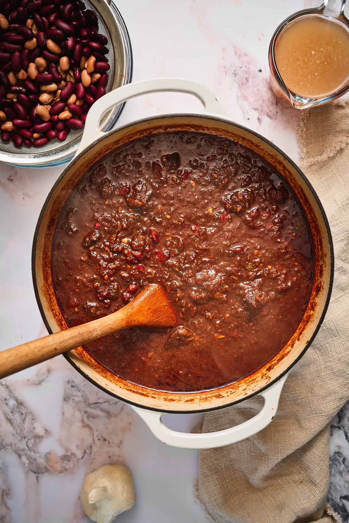 Chili that has simmered for hours and deepened in color with beans on the side getting ready to get added in.