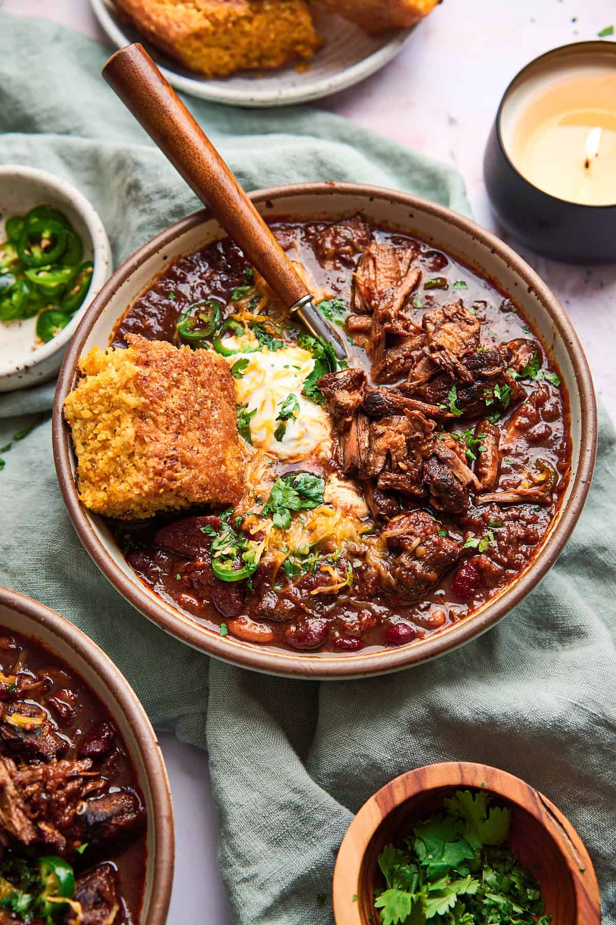Bowl of beefy chuck roast chili in a super savory rich tomato broth with beans and topped with sour cream, jalapenos, cheese, and green onions.