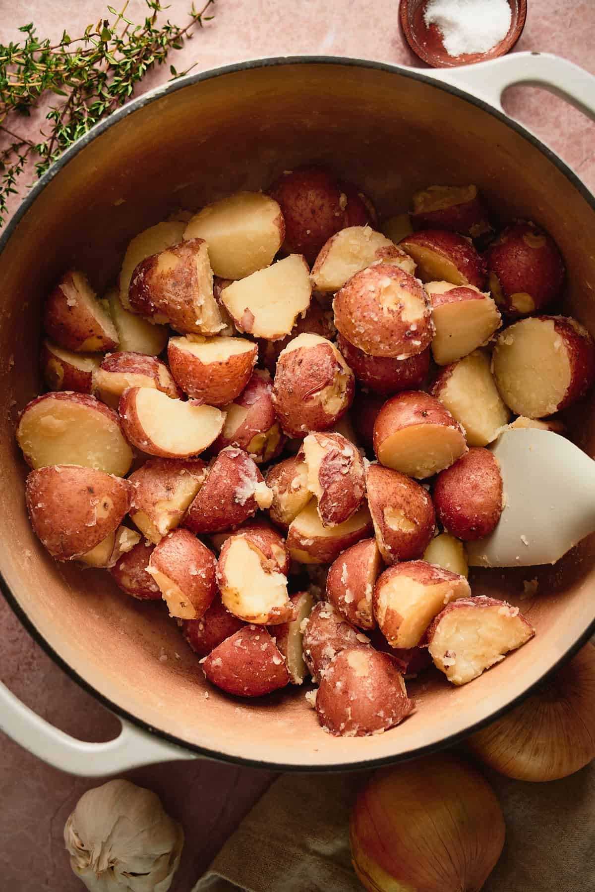 Potatoes that have been warmed in a Dutch oven, with the skin beginning to fall off, with a rubber spatula in the Dutch oven. 