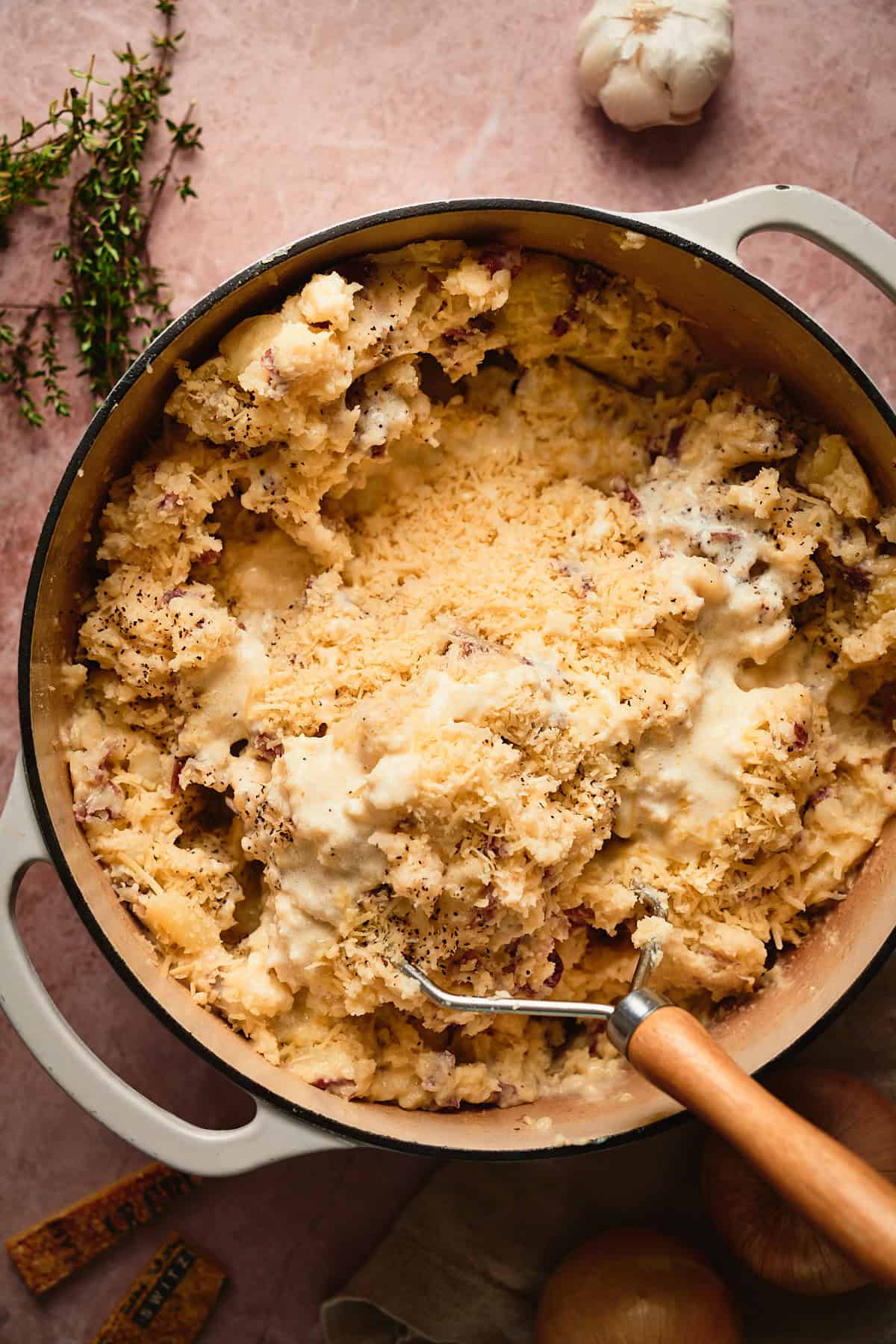 Mashing potatoes in a large Dutch oven with a hand masher, with cheese and cream added to the potatoes. 