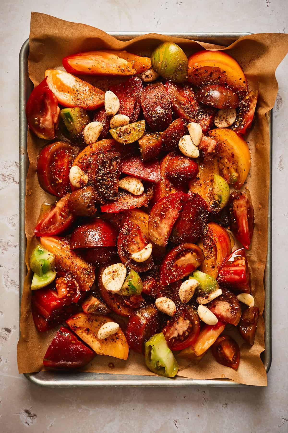 Tomatoes cut up on a pan and seasoned alongside garlic cloves. 