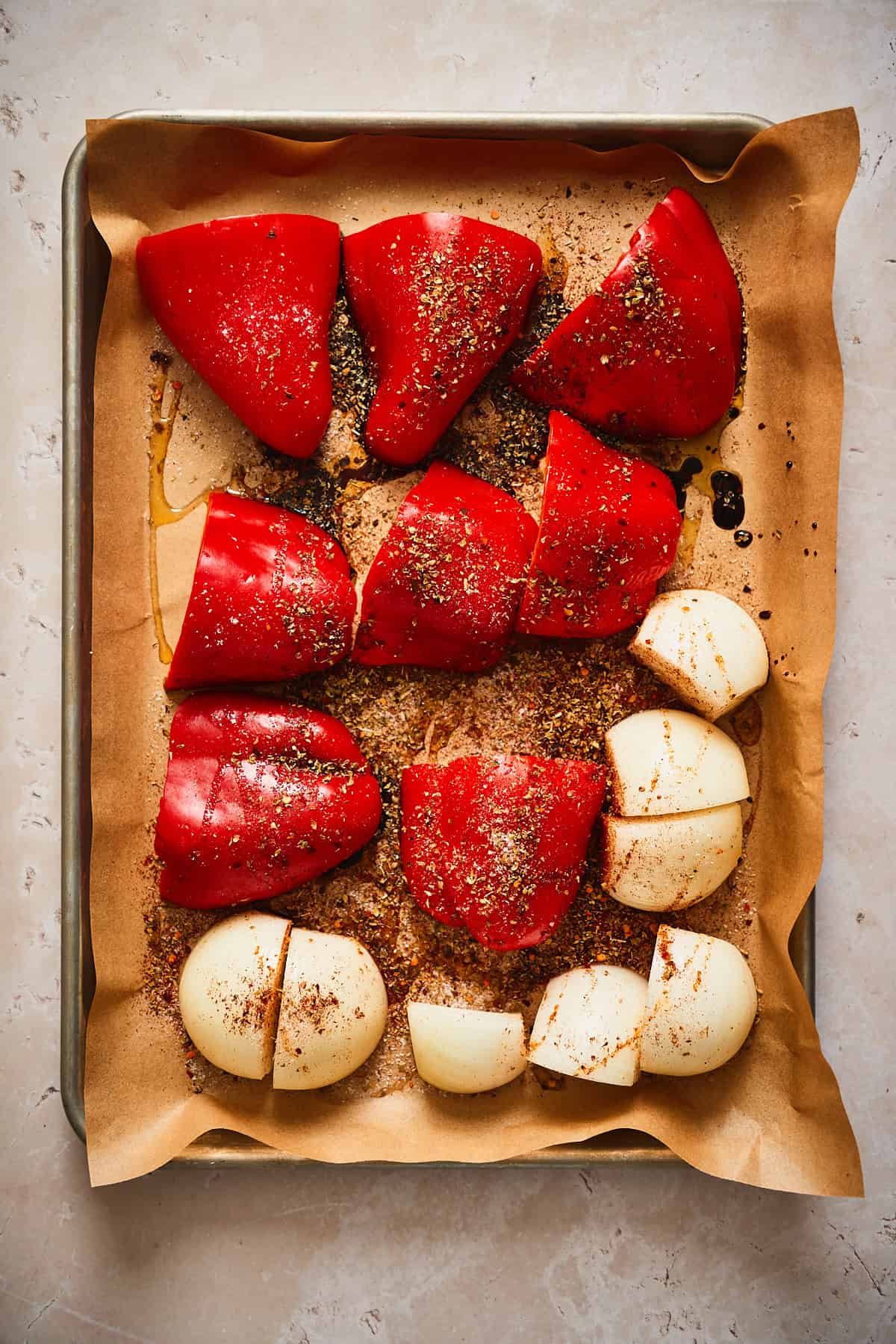 Red bell peppers and onions on a sheet pan covered with seasonings.  