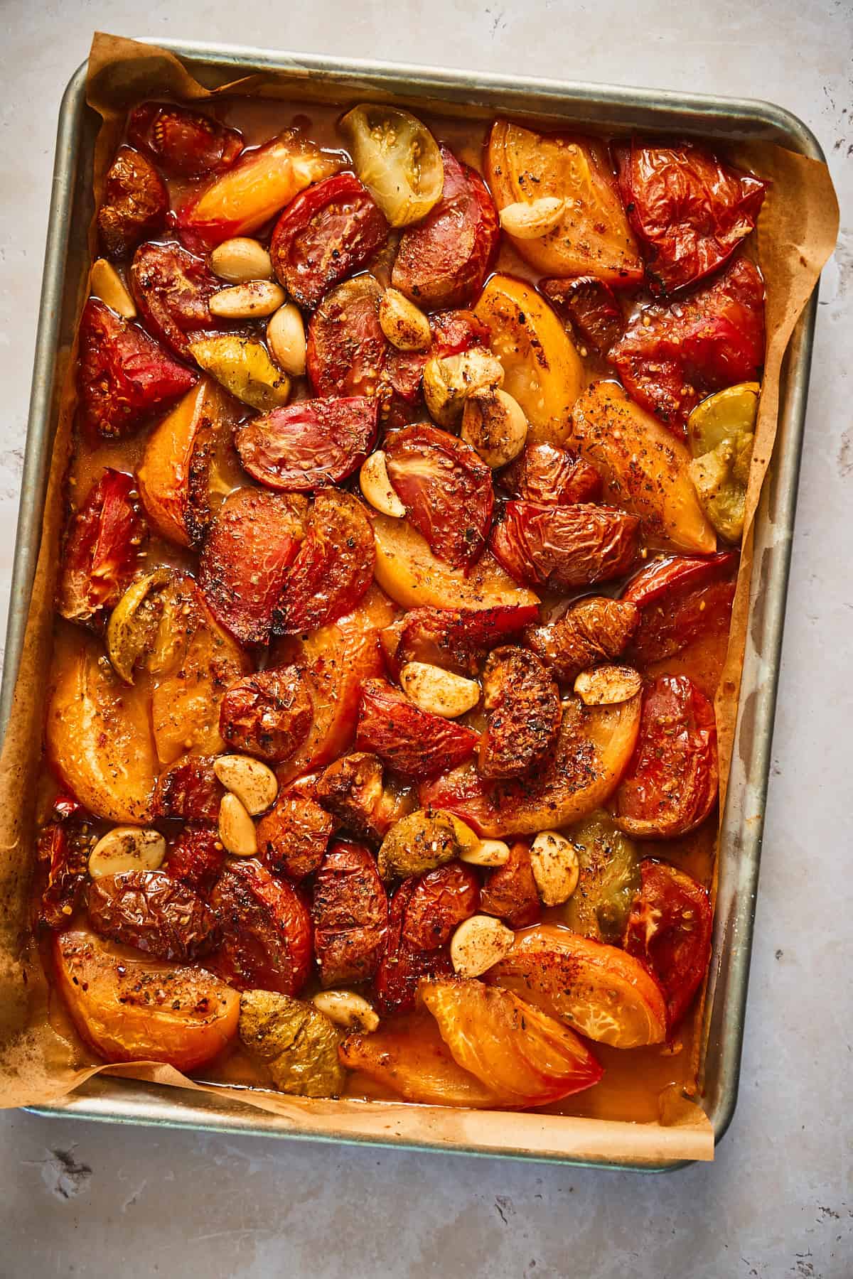Roasted tomatoes with garlic on a pan with bits of the tomatoes beginning to char. 