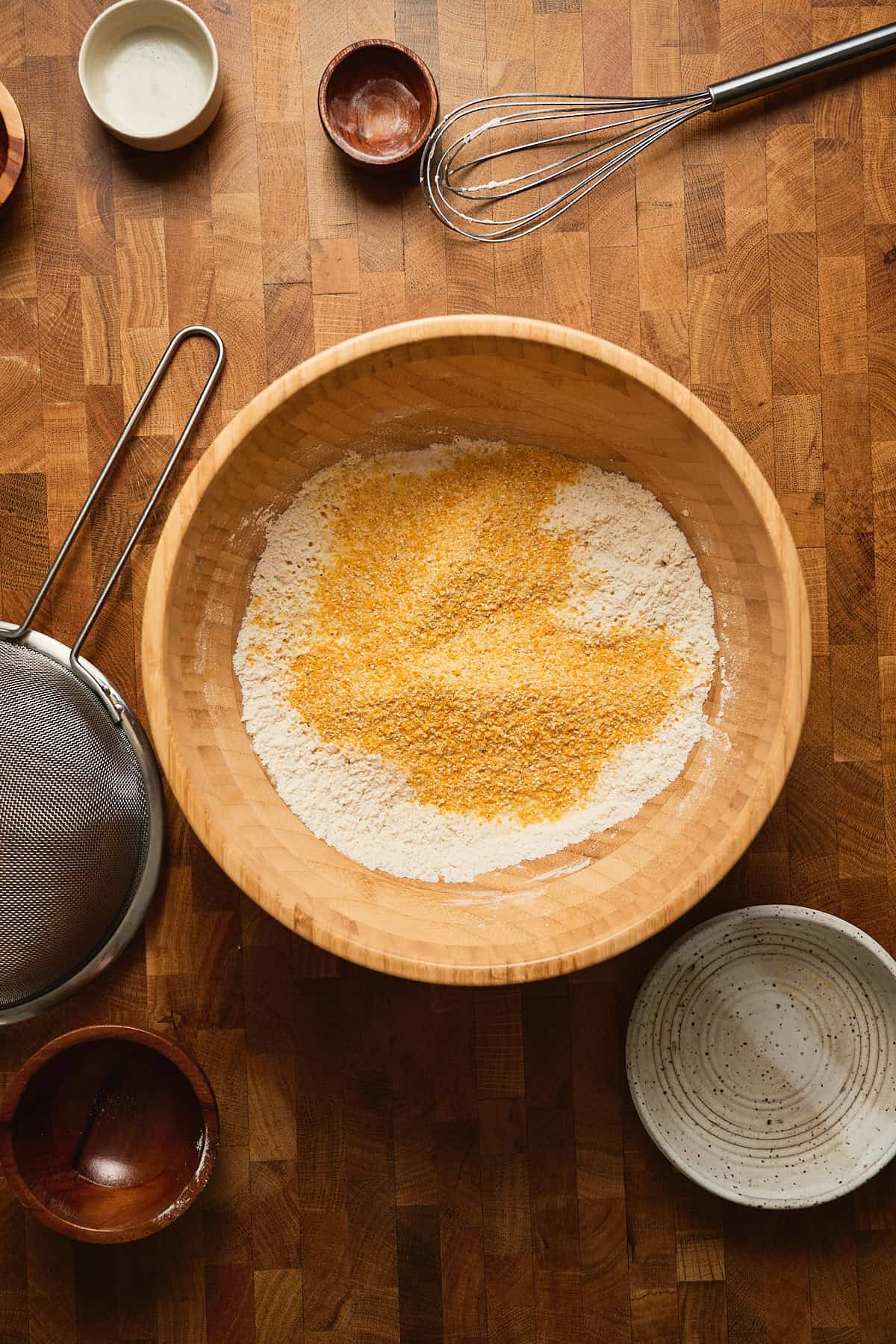 Mixing flour, cornmeal, and spices in a wooden bowl on a rustic kitchen countertop.