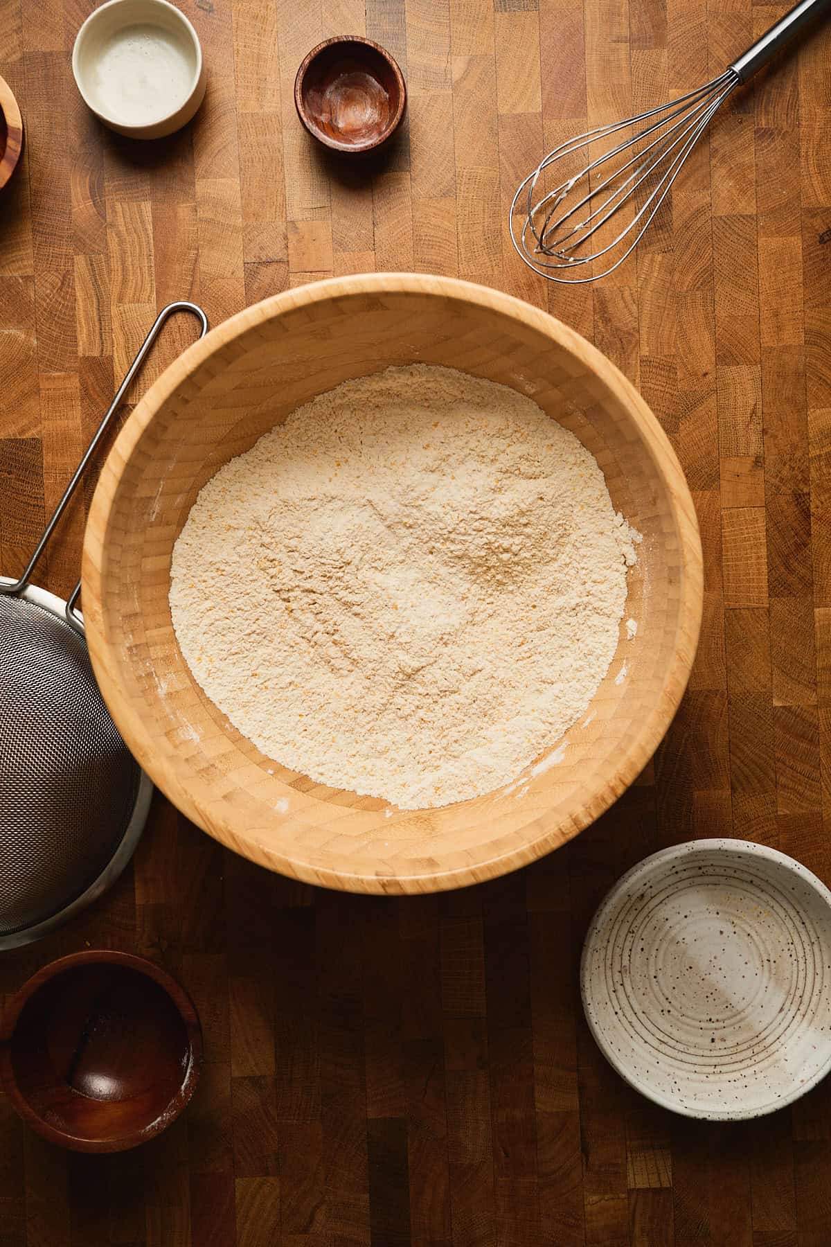 Flour in a wooden bowl with baking ingredients on a wooden countertop.
