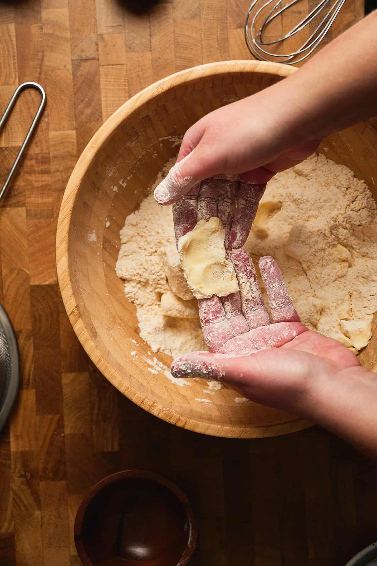 Hands pressing chunks of butter into thin sheets in a bowl full of dry ingredients.